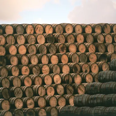 Hundreds of wooden whisky barrels are stacked on top of each other to form a large pile