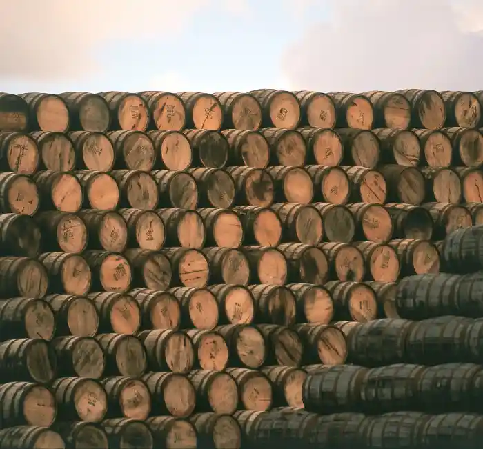 Hundreds of wooden whisky barrels are stacked on top of each other to form a large pile