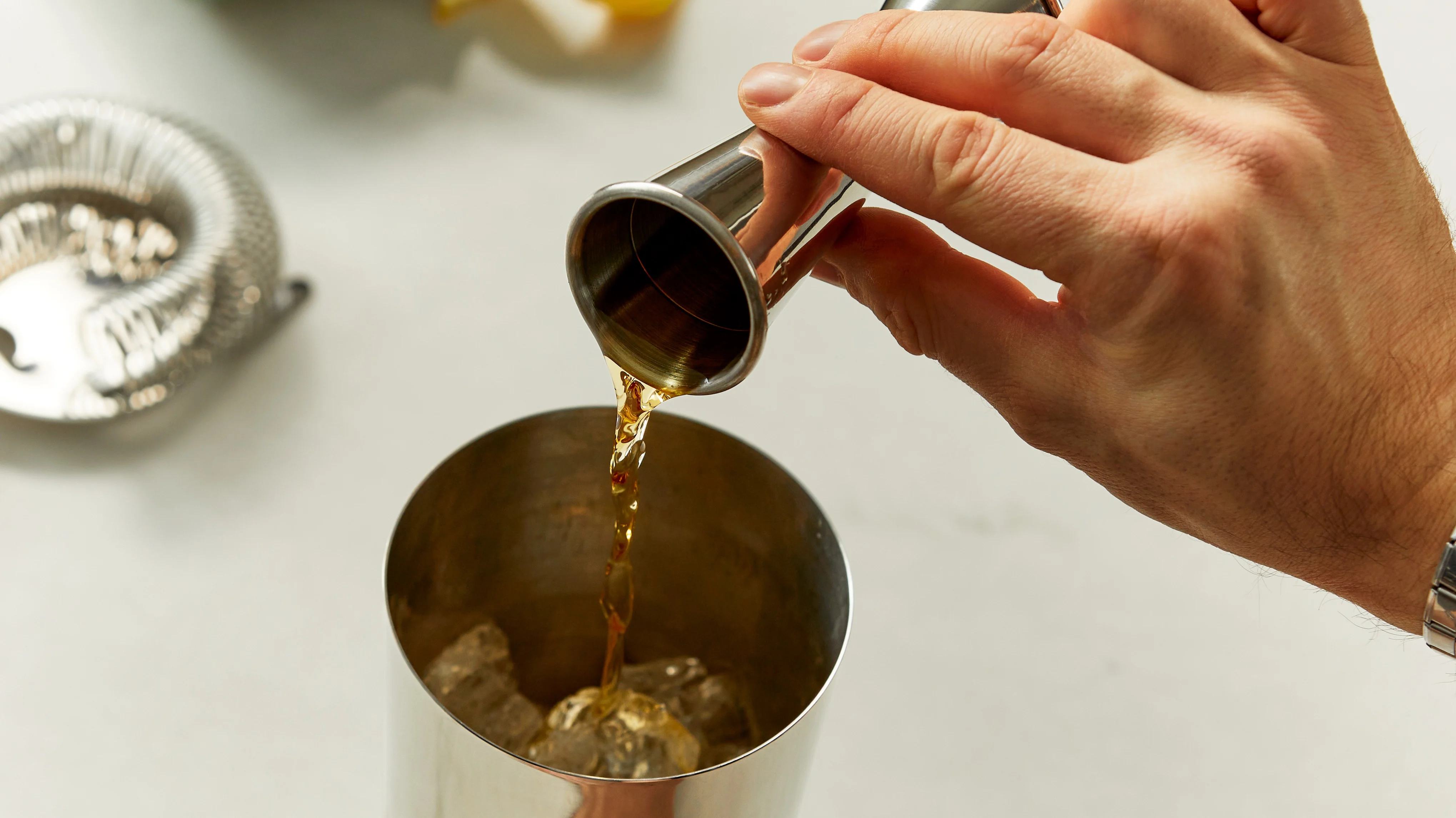 Whisky wird mit einem Jigger in einen Cocktailshaker gegossen