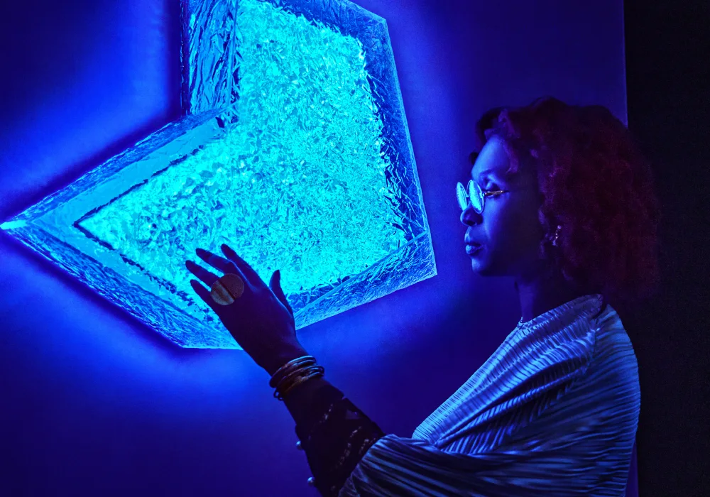 Een vrouw staat naast een neonblauw bord dat aan een muur is bevestigd en legt een hand op het bord.