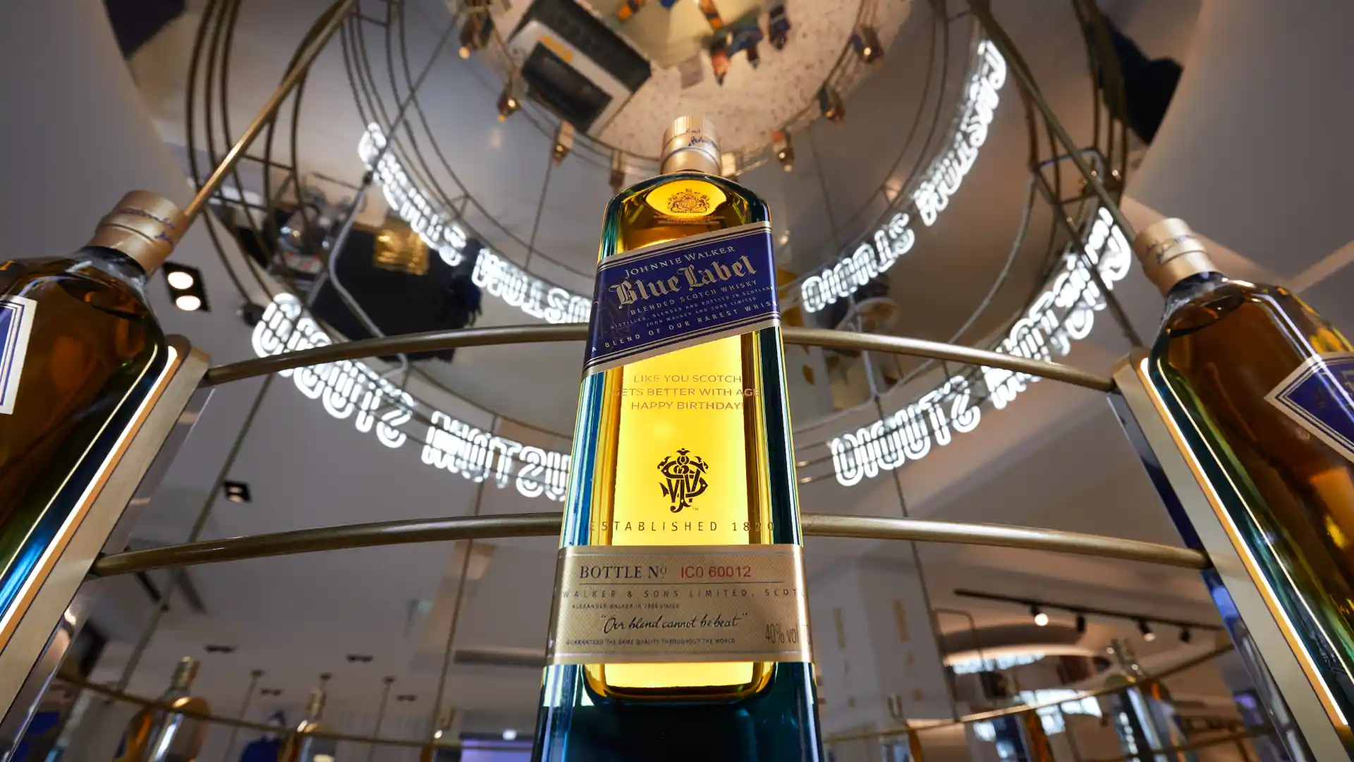  A bottle of Johnnie Walker Blue Label whisky sits on a plinth, with the camera focused upwards to show several floors of an inner atrium of a building behind the bottle.