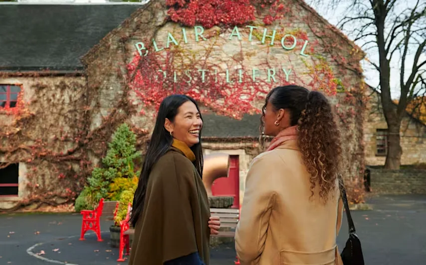 Two female friends stand outside Blair Athol distillery laughing and smiling