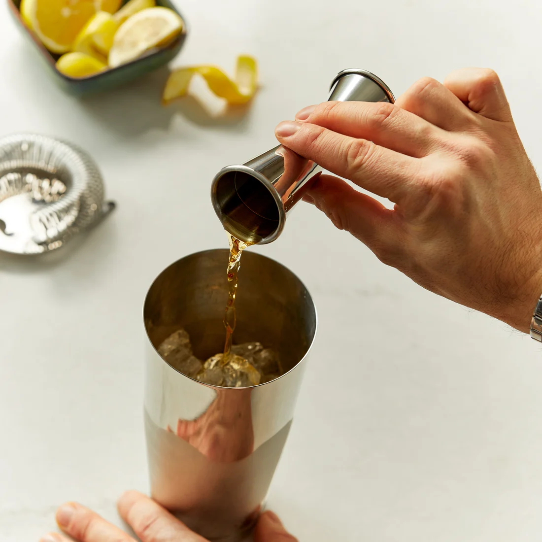 Een jigger giet een donkere sterke drank in een cocktailshaker gevuld met ijs.
