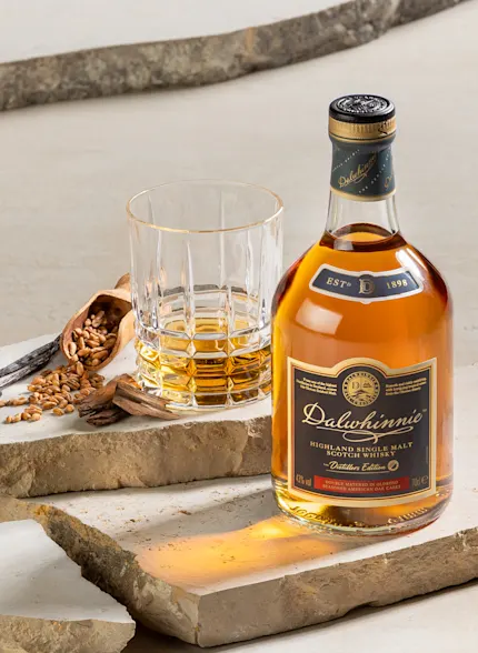 De Dalwhinnie Distillers Edition fles staat op een marmeren plaat naast een glas whisky met ijs en een assortiment whisky-ingrediënten.