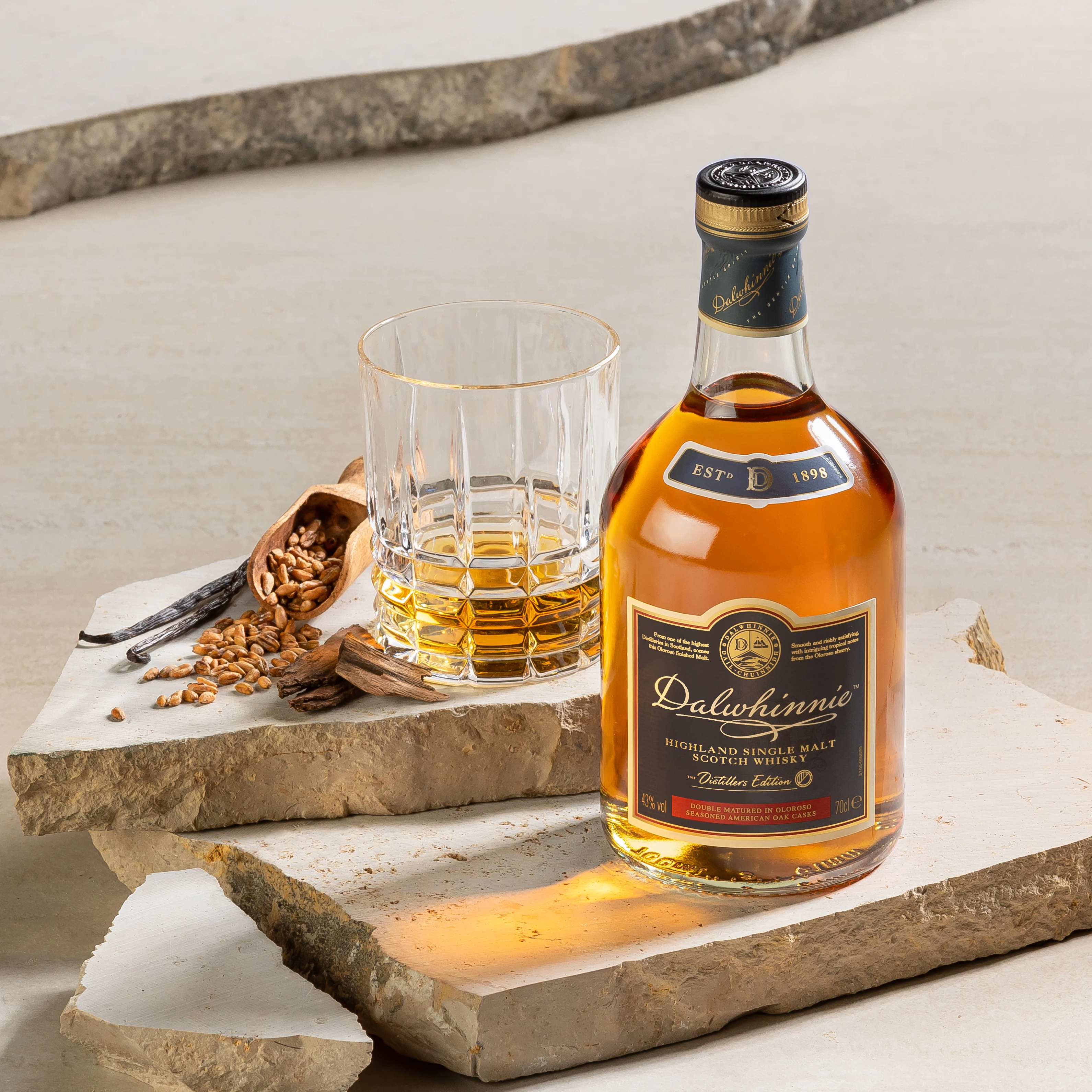 Dalwhinnie Distillers Edition bottle sits on a marble slab next to a rocks glass of whisky and an assortment of whisky ingredients