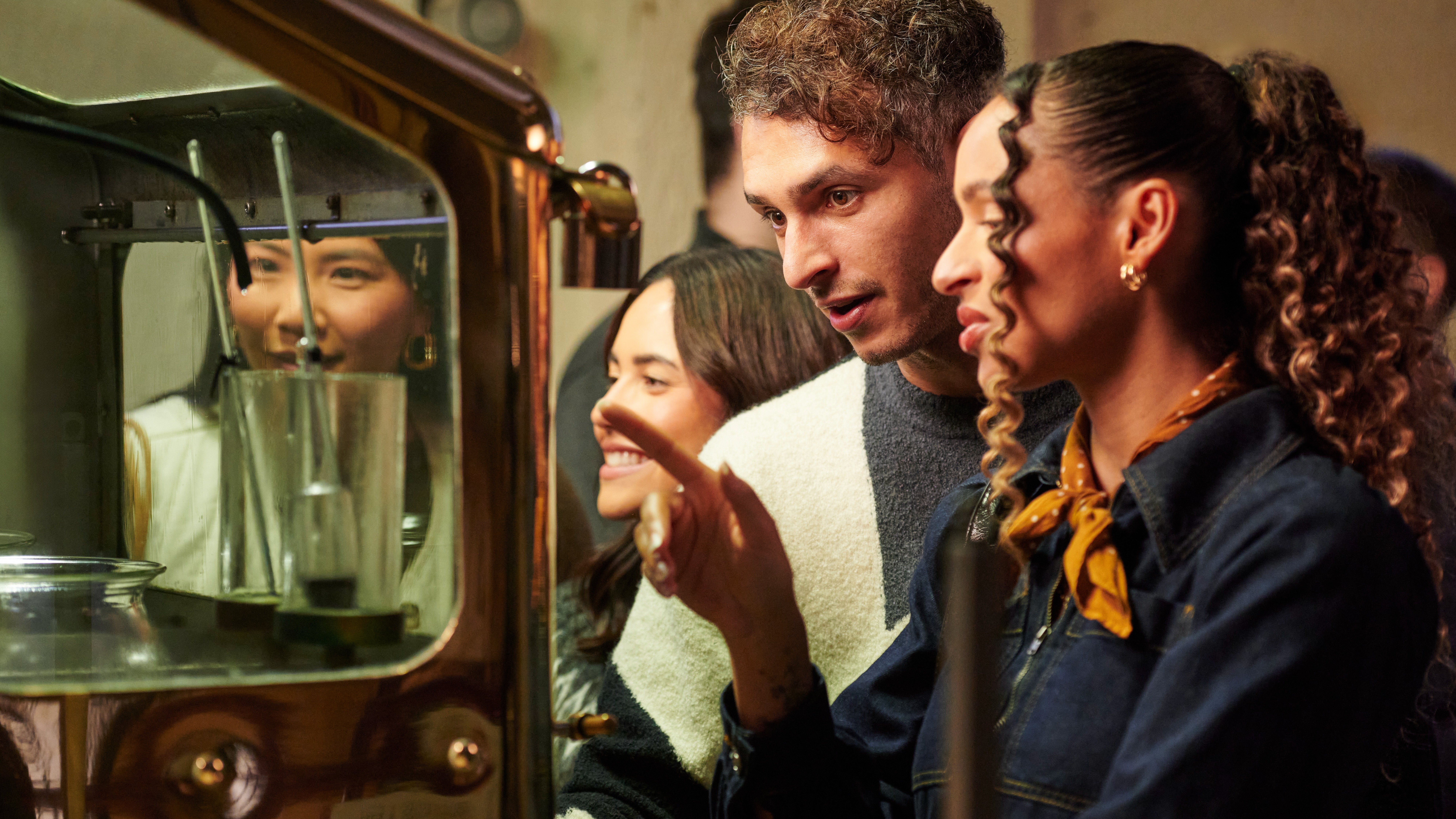 A tour group look into the Oban spirit safe: a large machine made of metal and glass through which whisky passes.