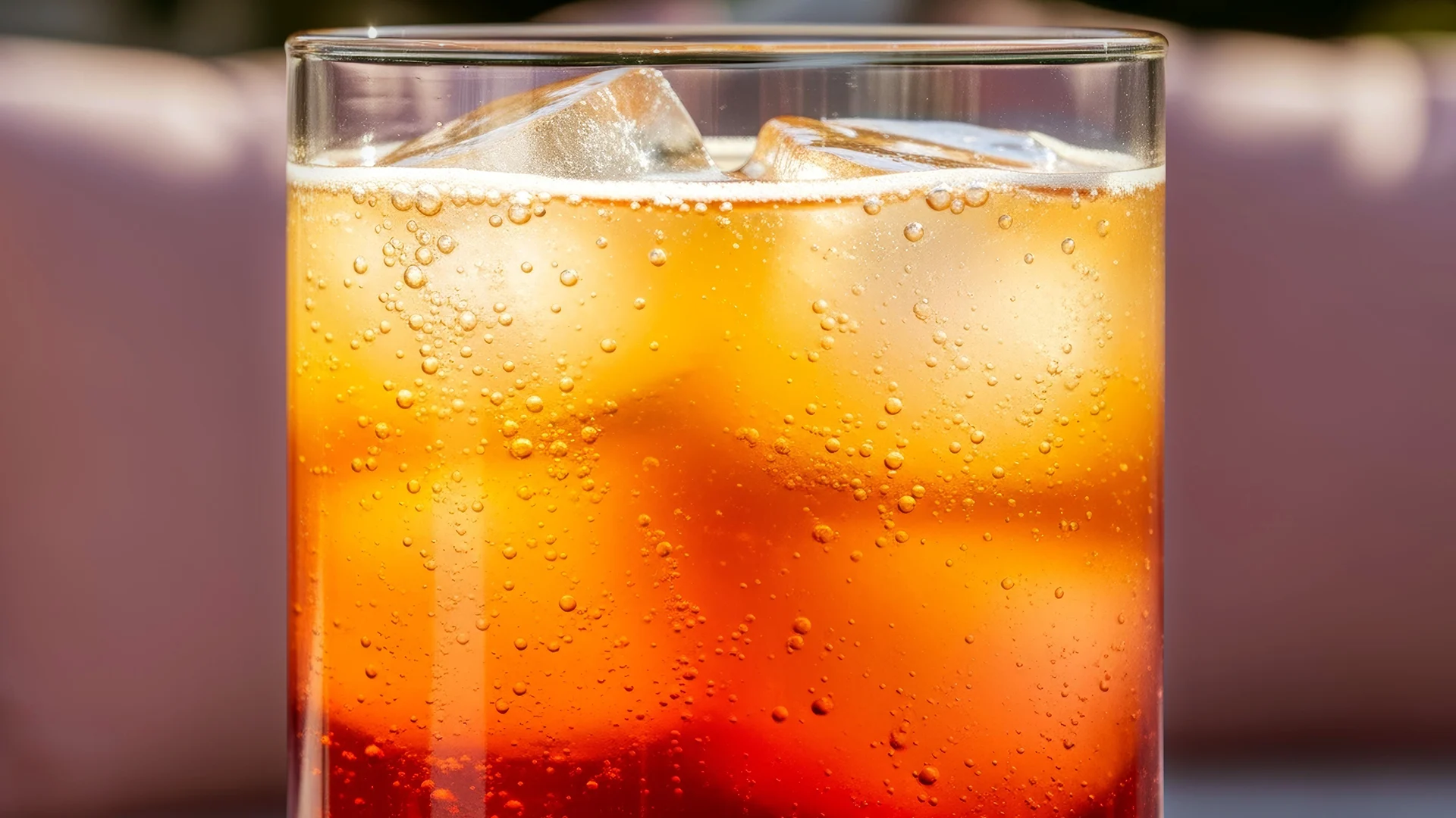 A close up of a light brown liquid in a highball glass with ice cubes, and bubbles.