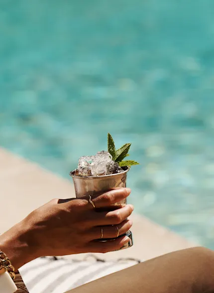 Eine Frau hält einen Mint-Julep-Cocktail in der Hand, während sie an einem Pool sitzt