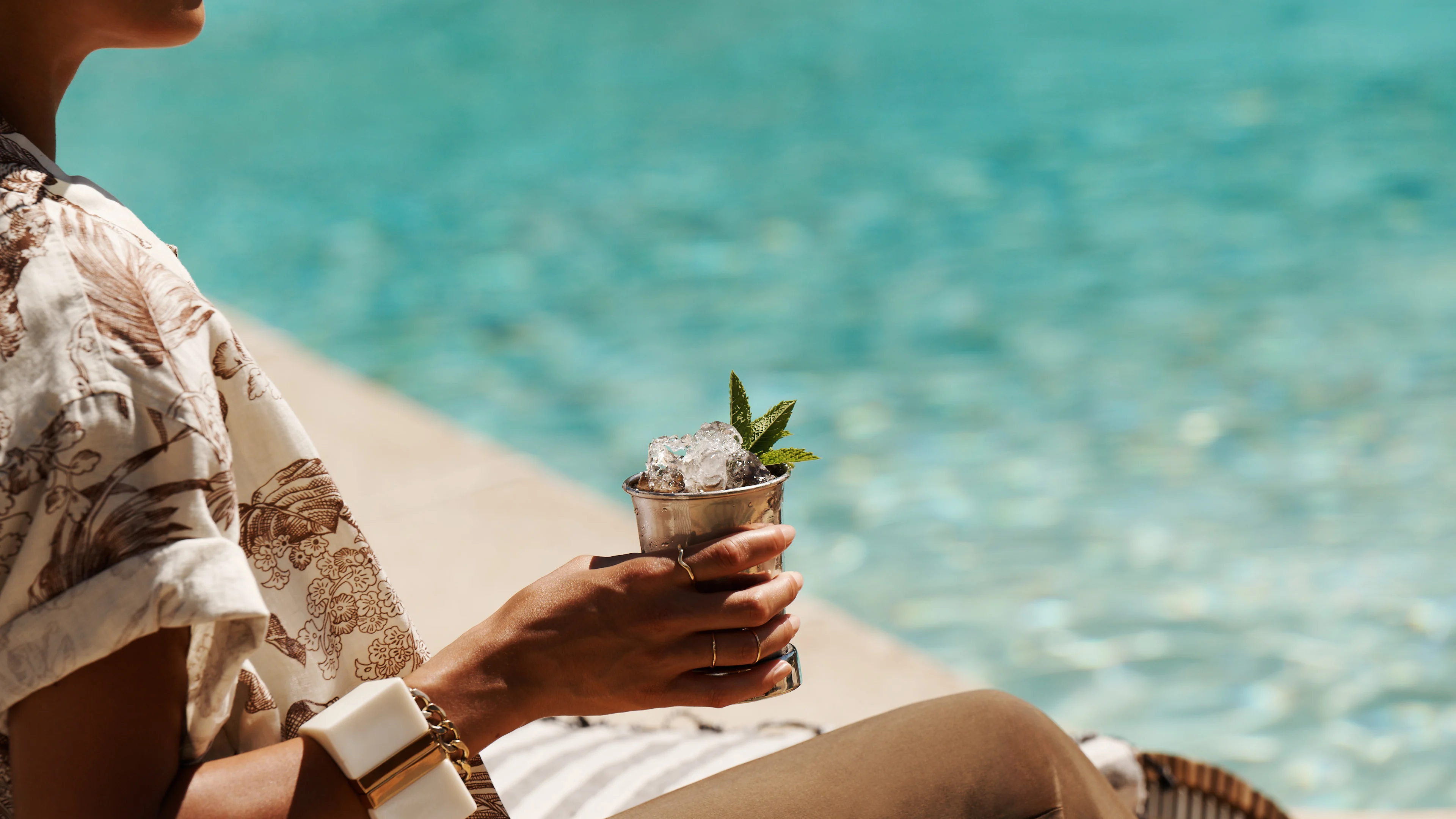 Eine Frau hält einen Mint-Julep-Cocktail in der Hand, während sie an einem Pool sitzt