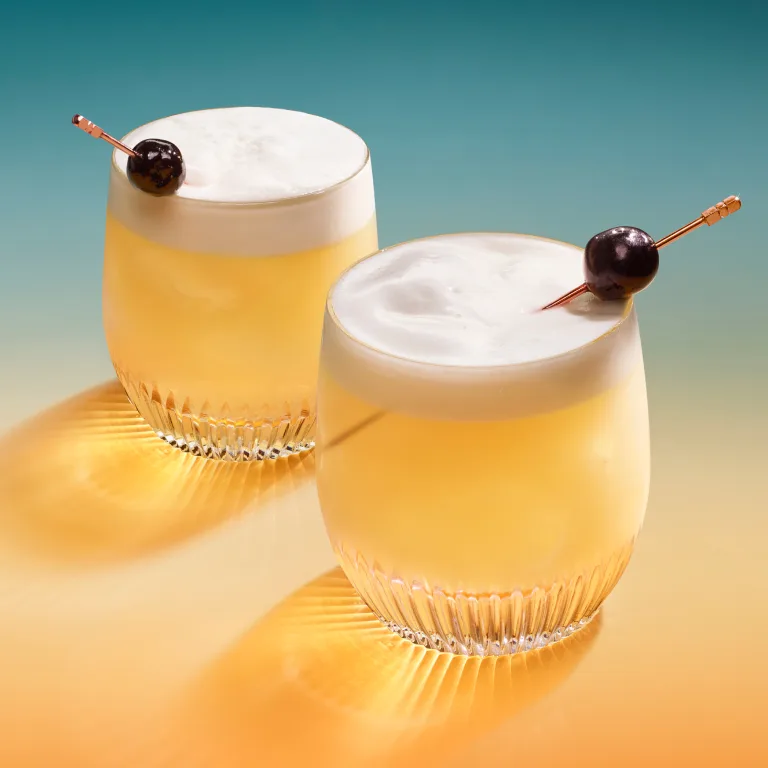 Two sour cocktails in rocks glasses with skewered maraschino cherry garnishes