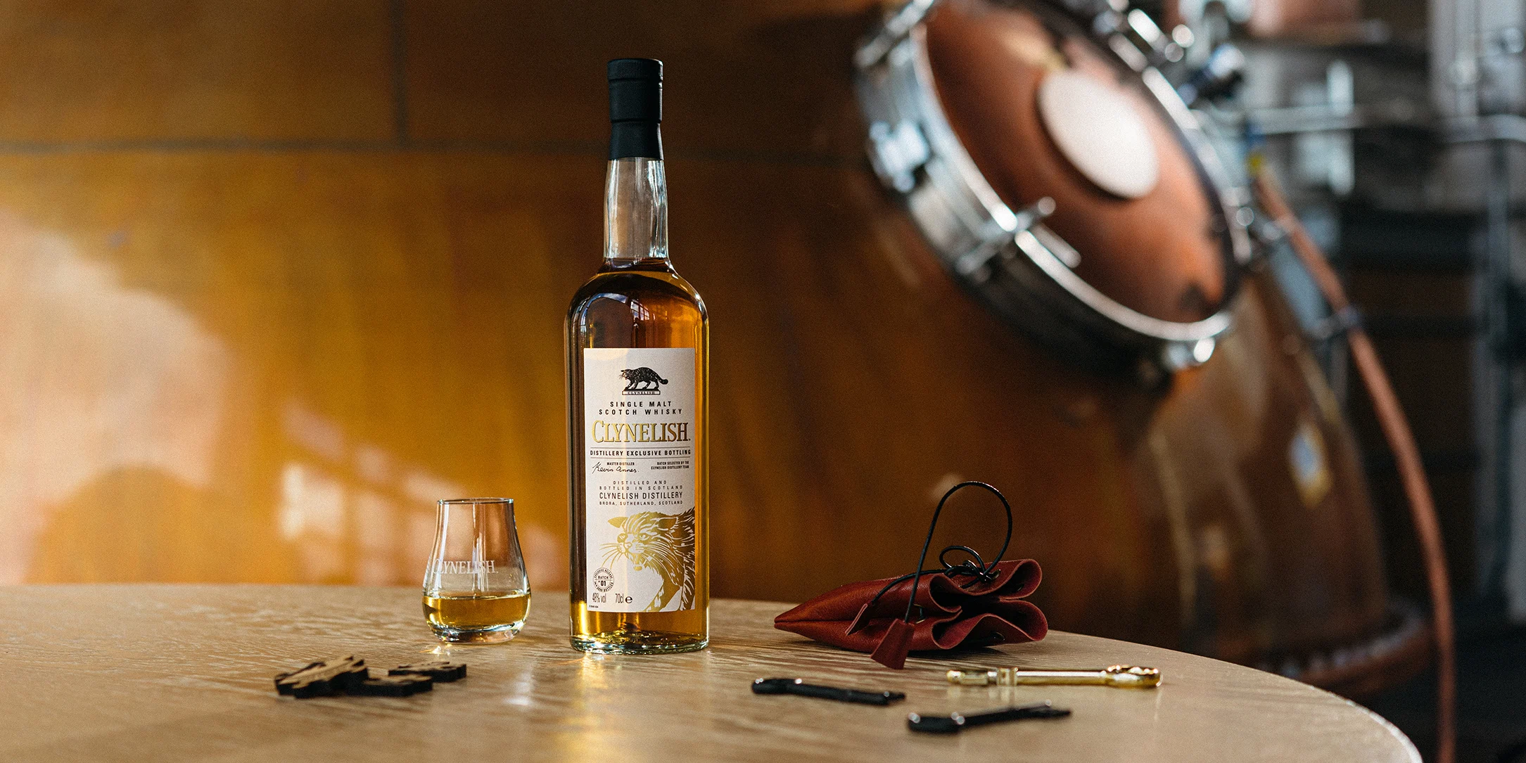 Placed on a wooden table, a bottle of Clynelish whisky, salame, cheese and bread platter, a lovely cocktail and a small dram