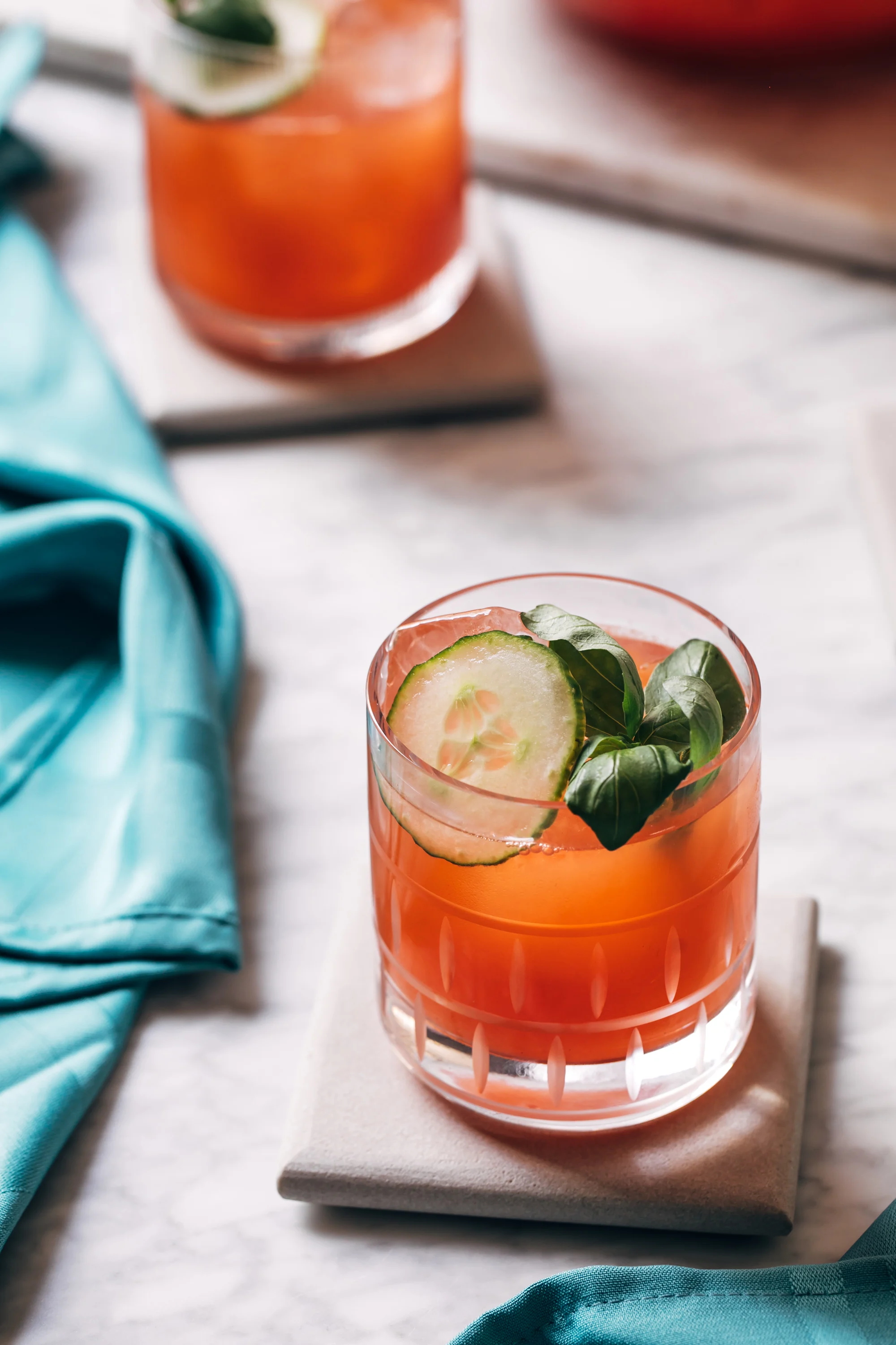 A pink cocktail in a rocks glass with ice and a cucumber garnish.