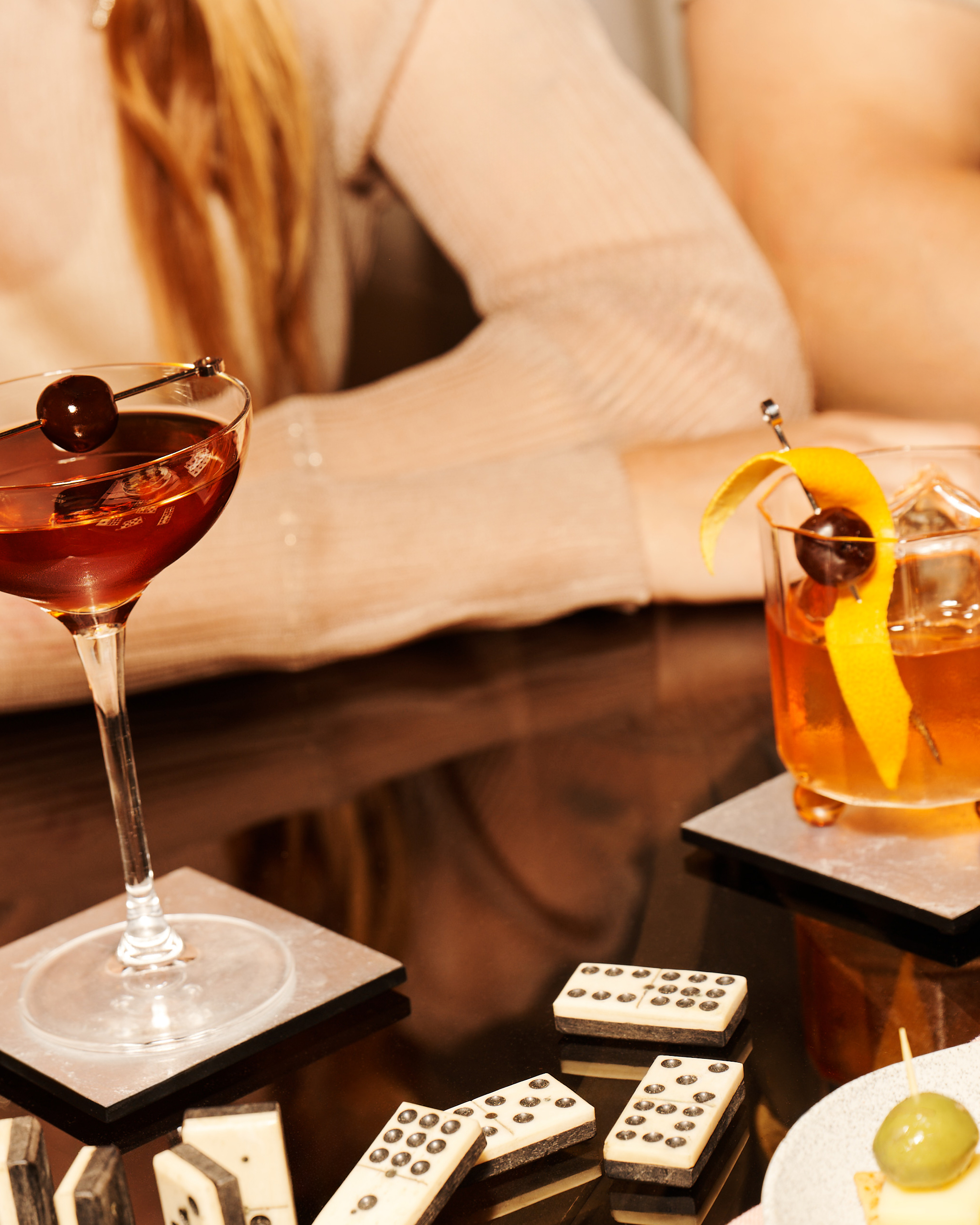 Zwei Old Fashioned-Cocktails und ein Manhattan-Cocktail stehen auf einem Glastisch