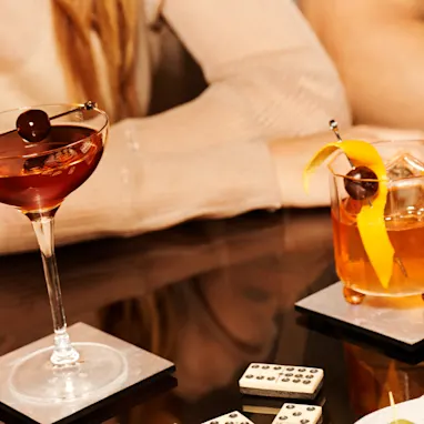 Two Old Fashioned cocktails and a Manhattan cocktail sit on a glass table
