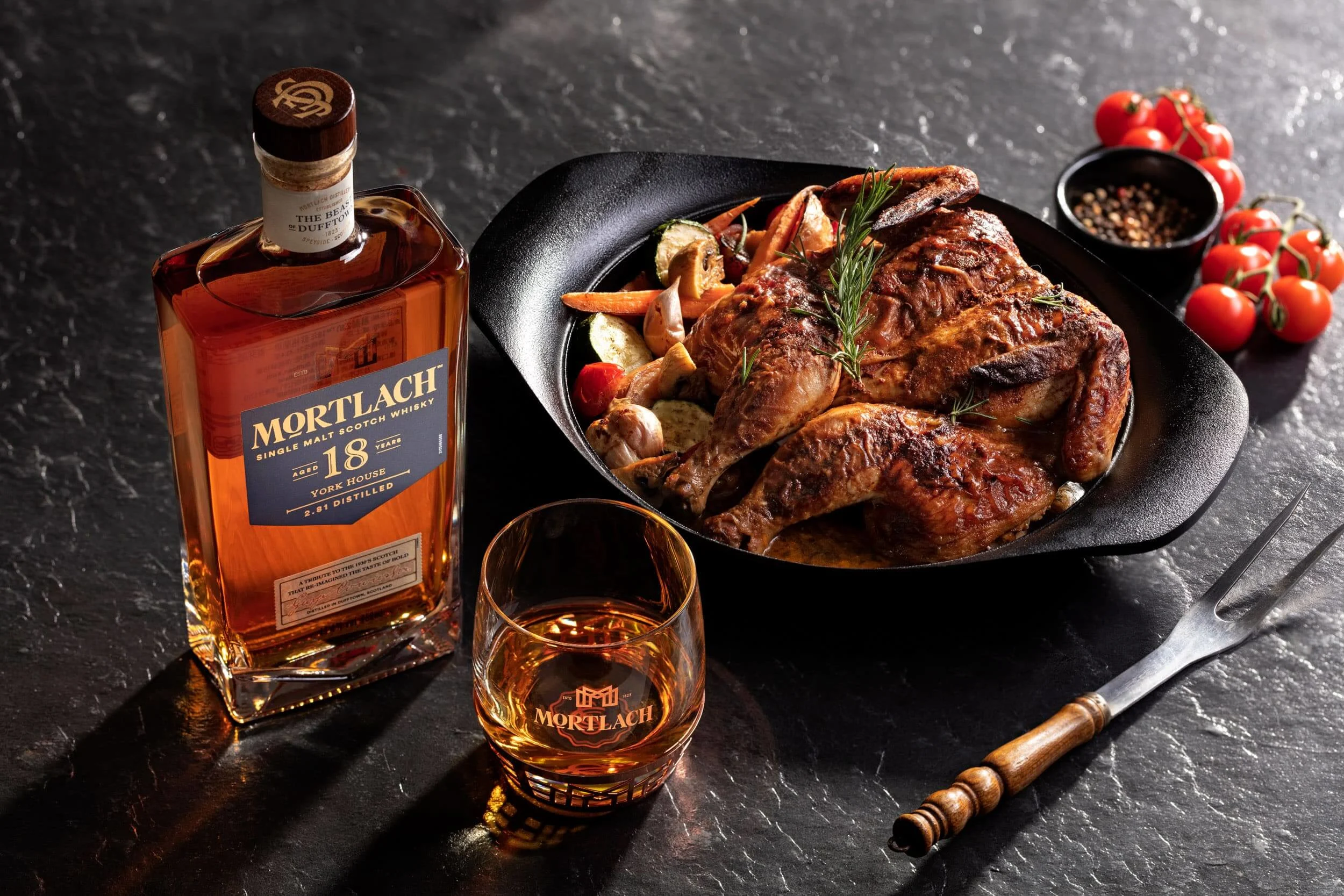 一瓶18年 Mortlach 威士忌、一杯威士忌和一盤精緻的雞肉料理放在桌子上。