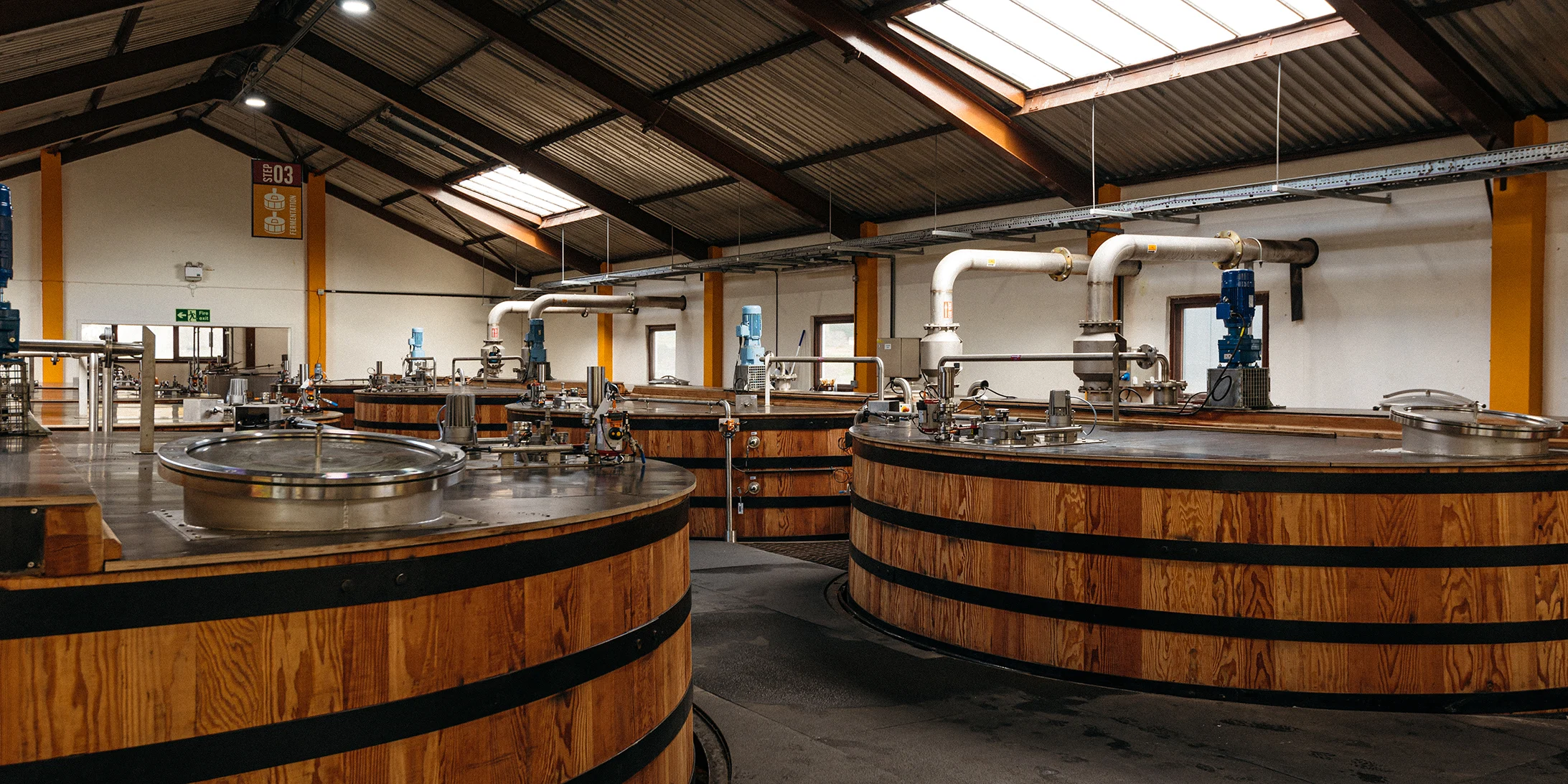 Interior of Clynelish Distillery showing large wooden-clad stainless steel fermentation washbacks inside a bright, modern production facility in the Scottish Highlands