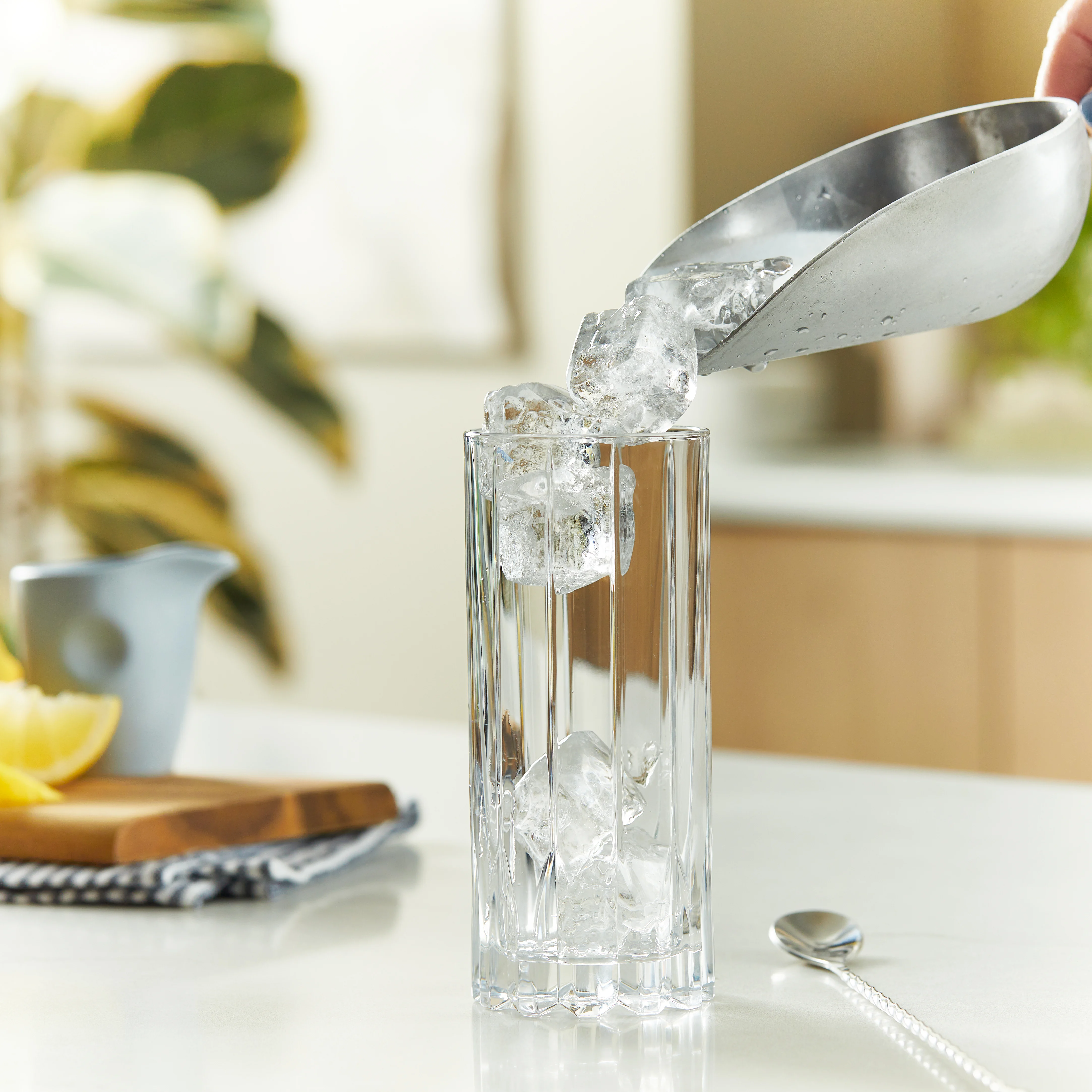Square ice cubes being poured into a clear highball glass.