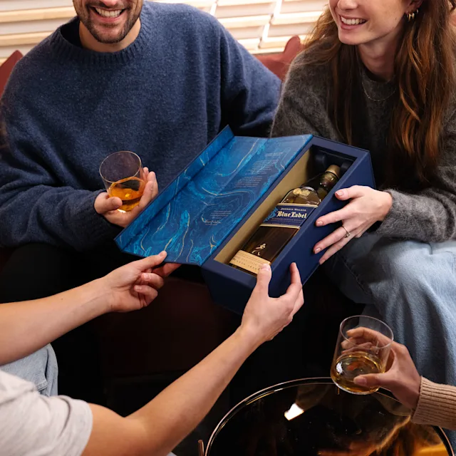 Eine kleine und gemütliche gesellschaftliche Umgebung. Eine Flasche Johnnie Walker Blue Label in der offenen Box wird in die Mitte der Gruppe gehalten. Eine Flasche Johnnie Walker Blue Label in der offenen Box wird in die Mitte der Gruppe gehalten.