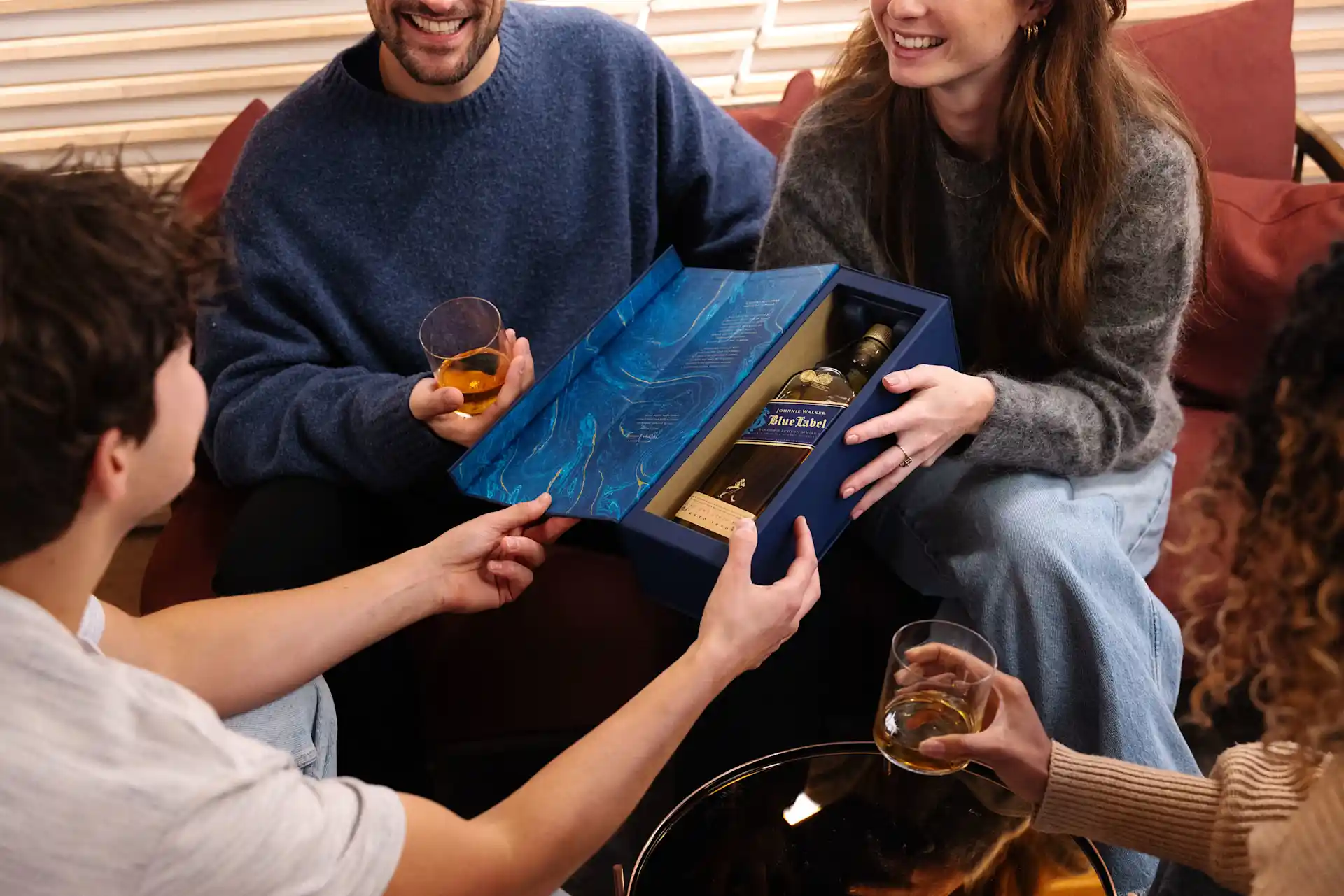 A small and comfortable social setting. A bottle of Johnnie Walker Blue Label in the open box is held in the middle of the group. A bottle of Johnnie Walker Blue Label in the open box is held in the middle of the group.