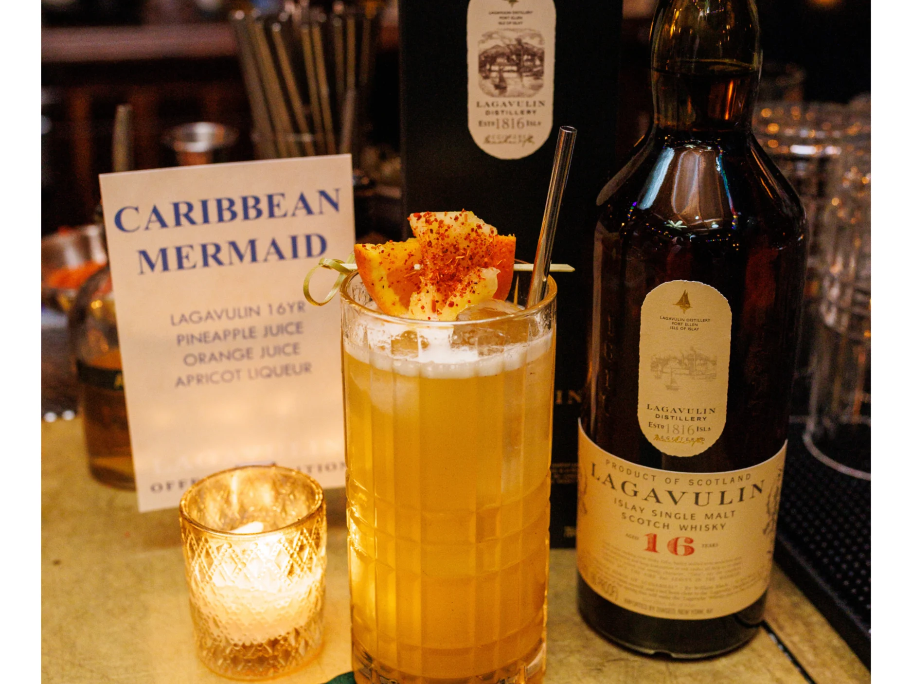Een Caribische cocktail in een highballglas met een fruitgarnituur naast een fles Lagavulin whisky.