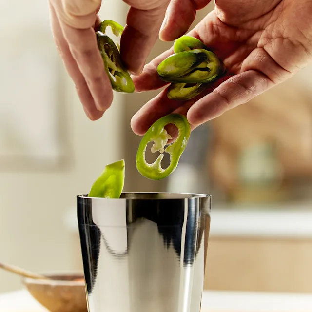 Verschillende plakjes jalapeno peper worden in een zilveren cocktailshaker gegooid
