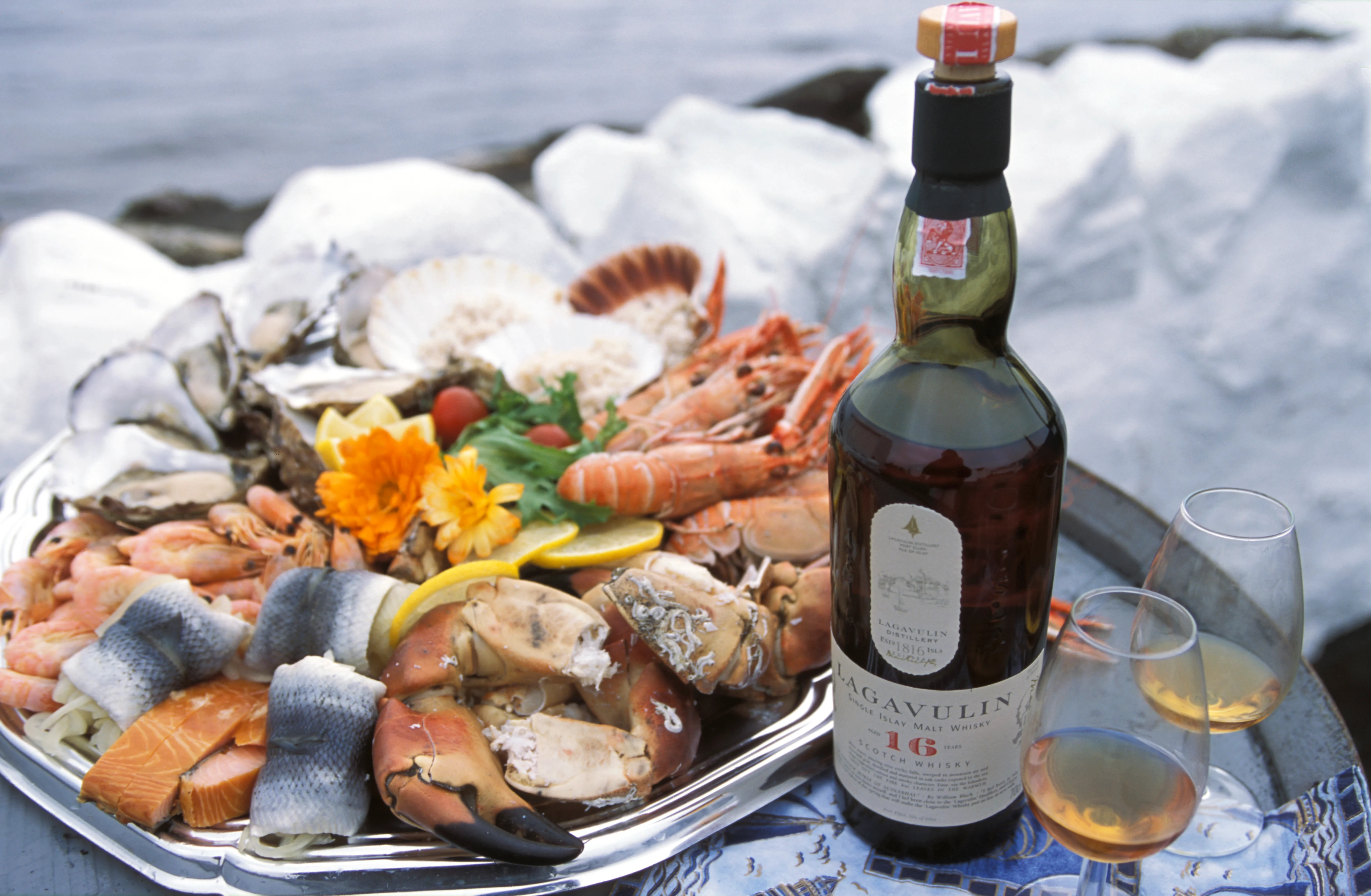 A platter of mixed seafood sits next to a bottle of Lagavulin 16 year old and two rocks glasses containing whisky