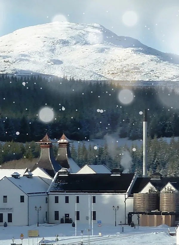 Outside view of Dalwhinnie Distillery with the mountains in the background covered with snow