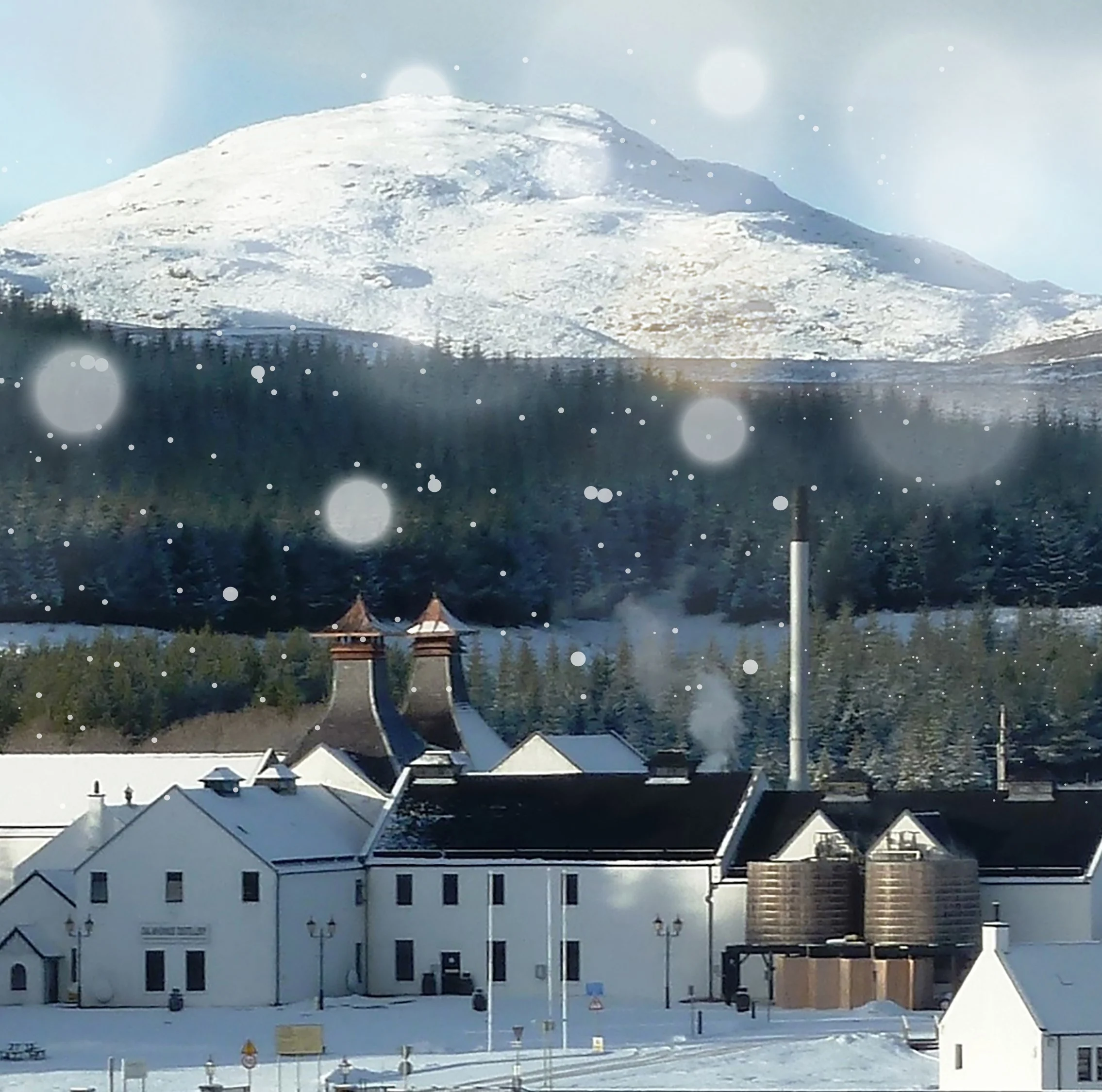 Outside view of Dalwhinnie Distillery with the mountains in the background covered with snow 