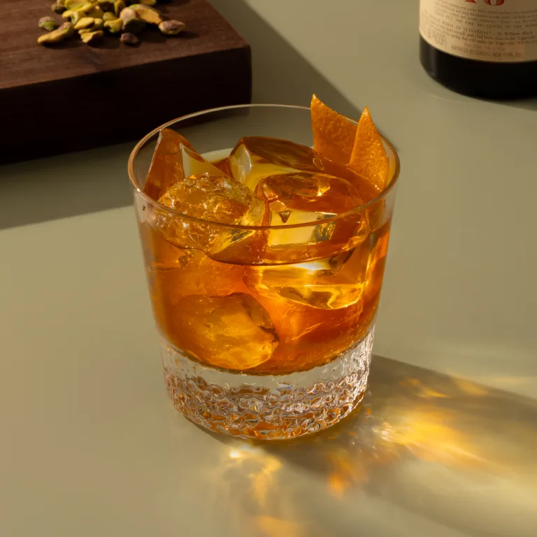 A cocktail in a rocks glass with ice and a large orange peel