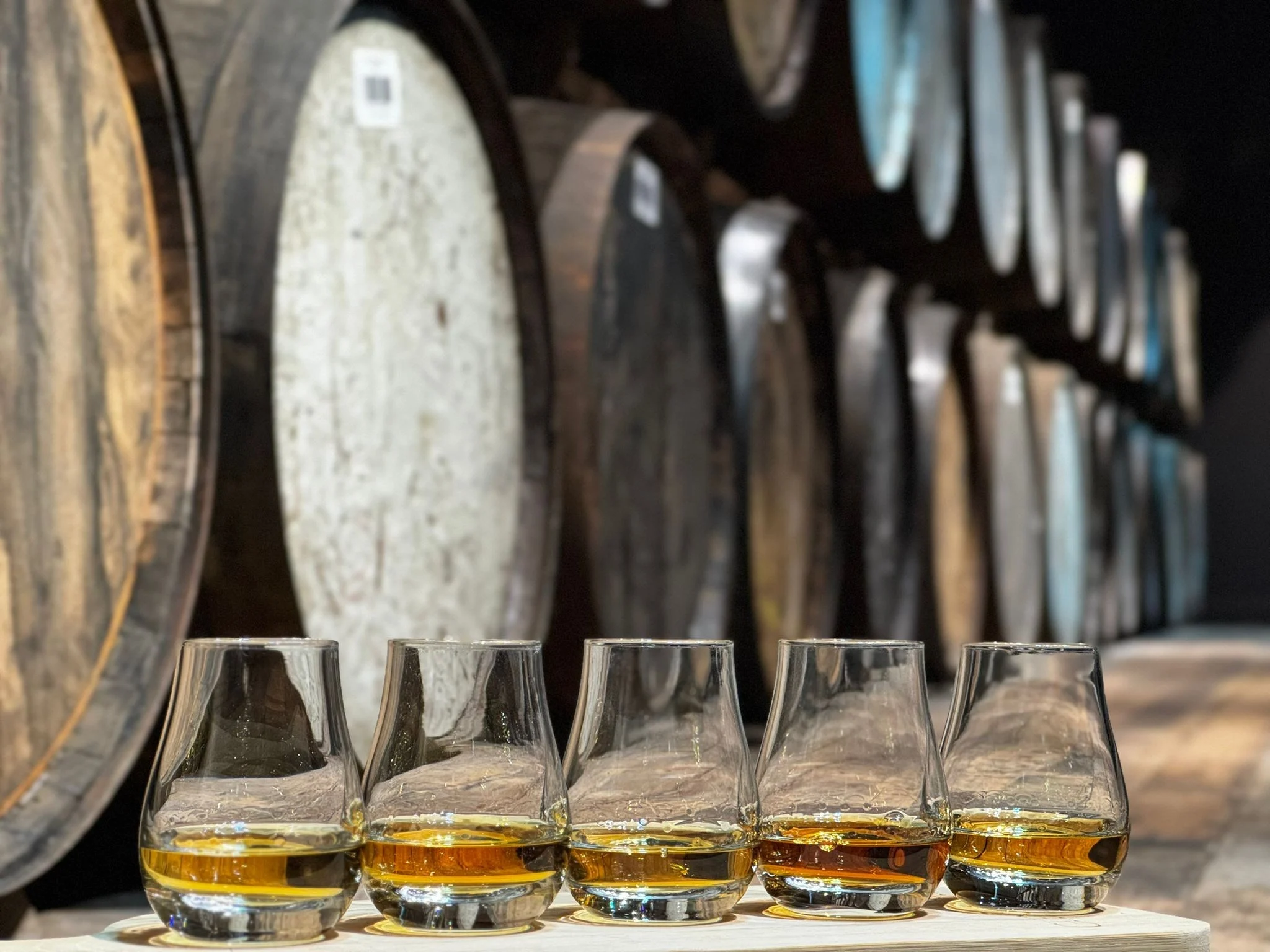 An Image of five whiskies with casks in the background