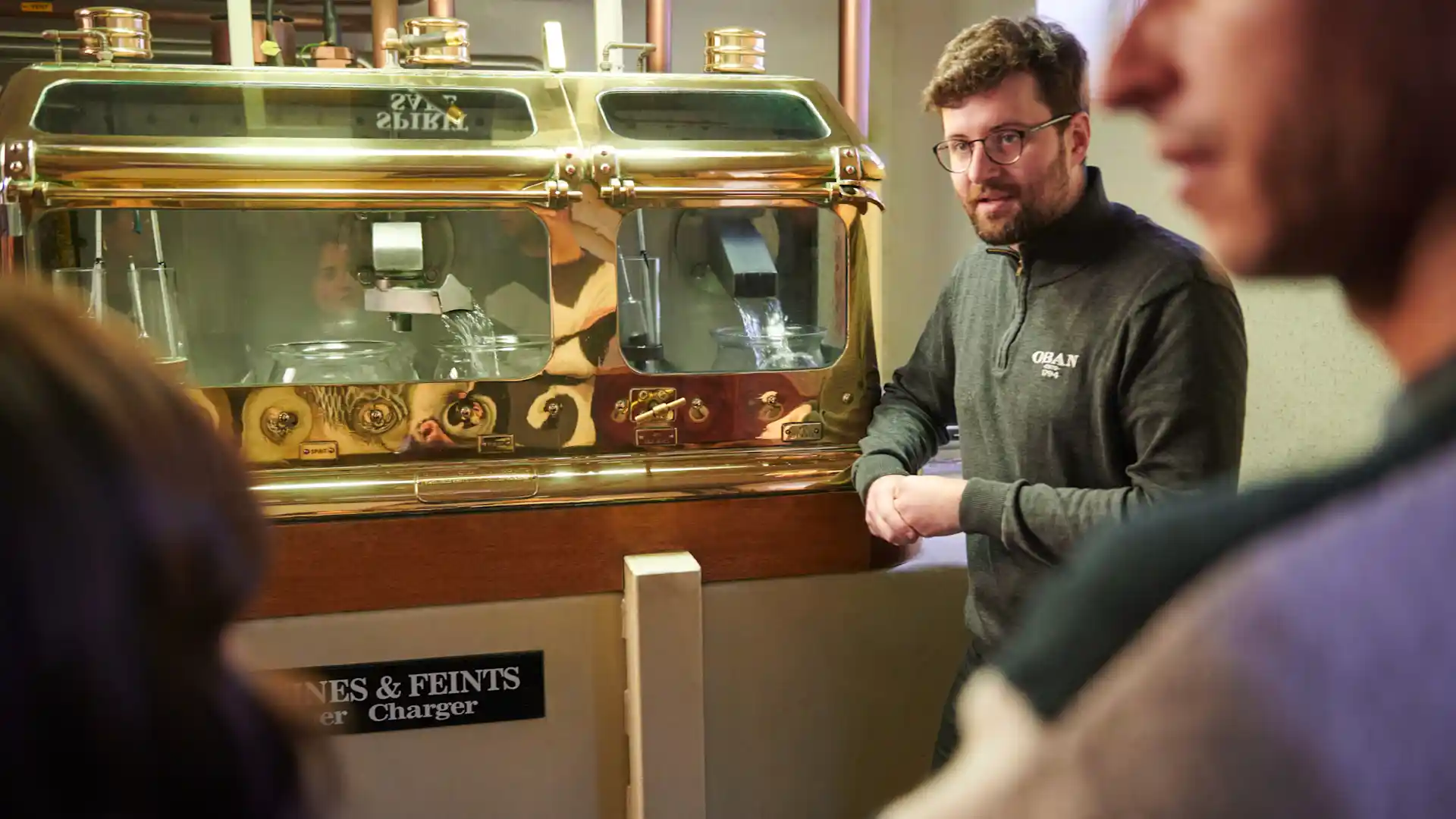 An Oban tour guide shows a tour group the spirit safe: a large, gold and glass machine through which whisky passes.