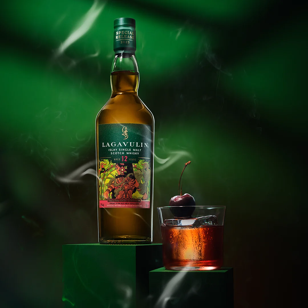 Shop smoky whisky A bottle of Lagavulin 12 year old whisky sits on a green plinth next to a rocks glass holding whisky and a cherry