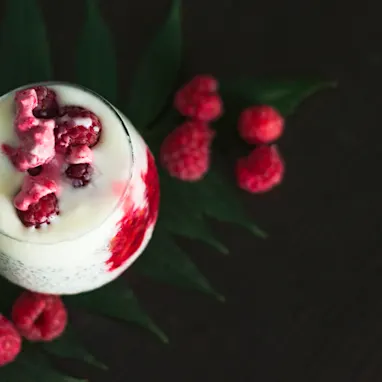 A creamy looking cocktail with fresh raspberries