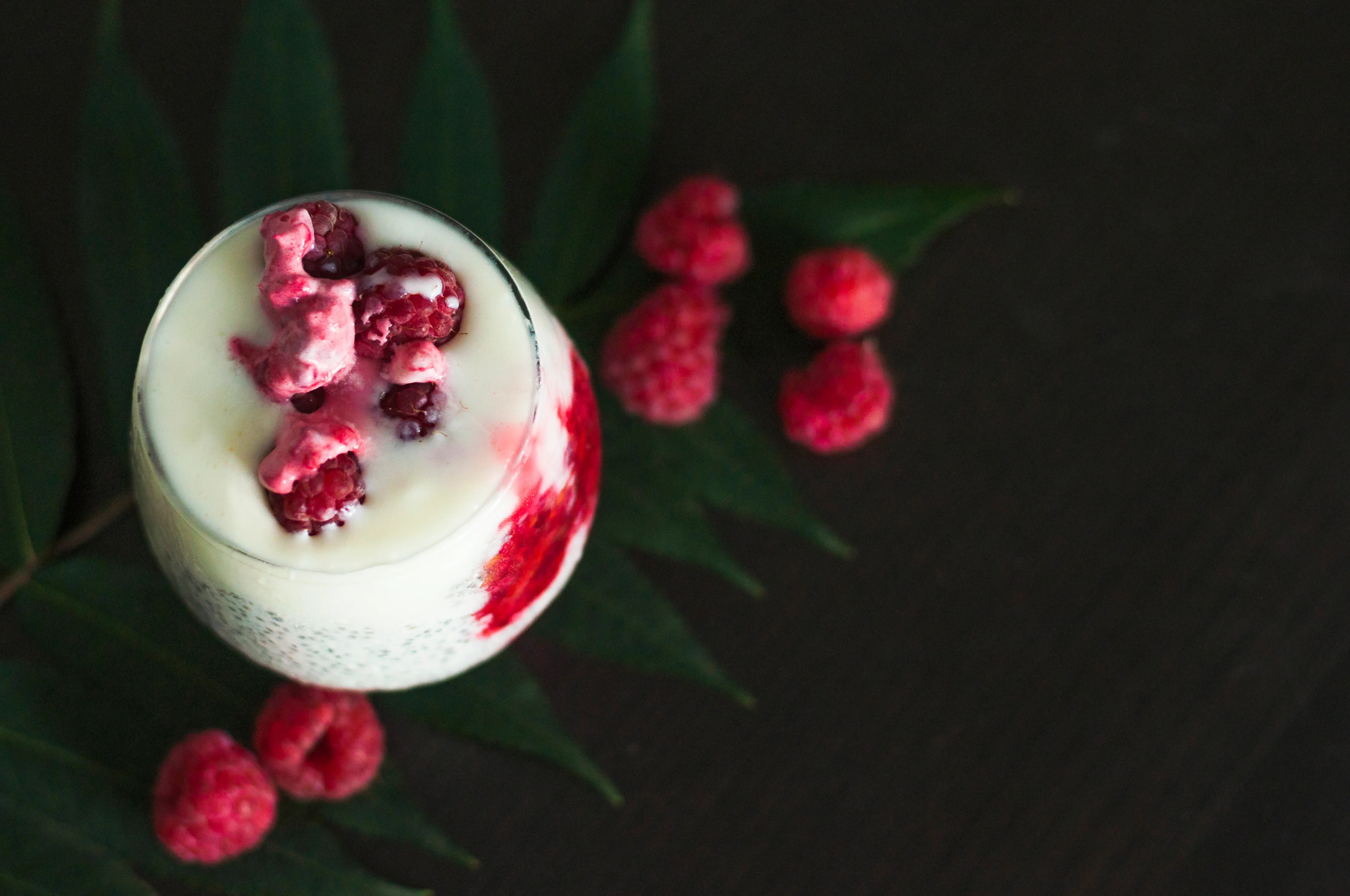 A creamy looking cocktail with fresh raspberries