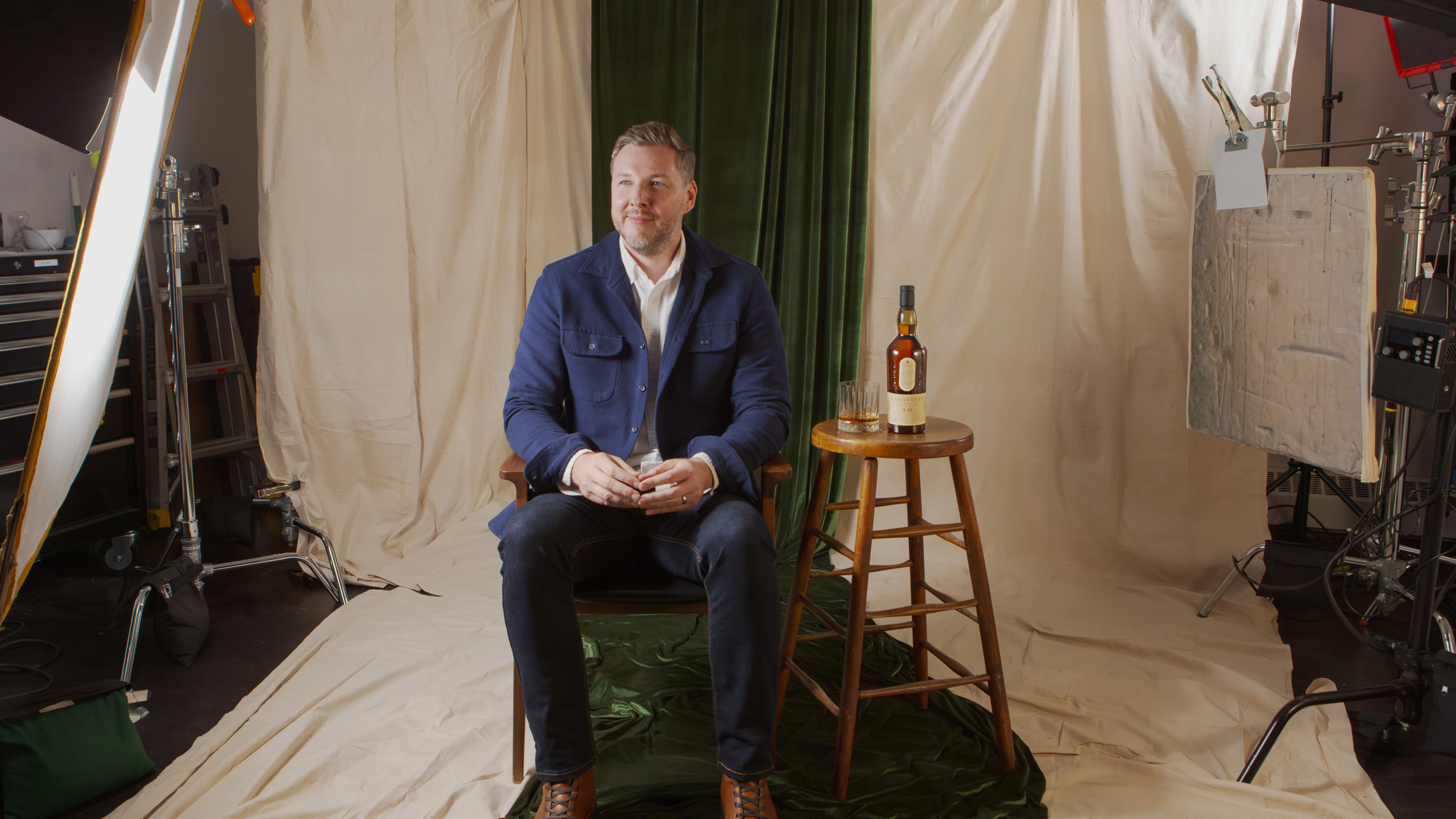 Greg King smiles as he sits beside a bottle of Lagavulin 16 Year and a rocks glass.