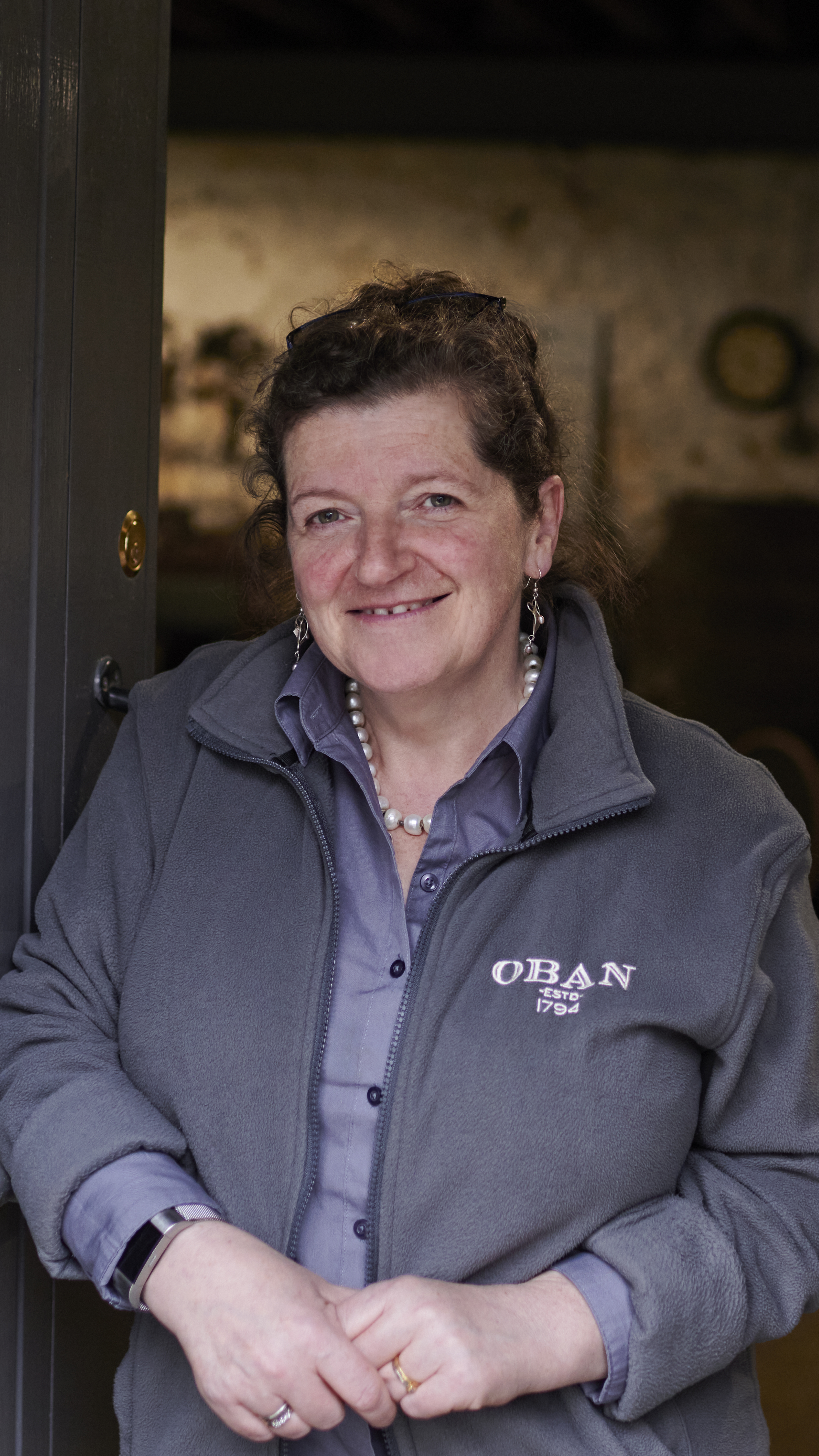 Lesley, een reisleidster van Oban, staat in een opslagruimte in de distilleerderij en draagt een grijze jas met het merk Oban.