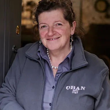 Lesley, een reisleidster van Oban, staat in een opslagruimte in de distilleerderij en draagt een grijze jas met het merk Oban.