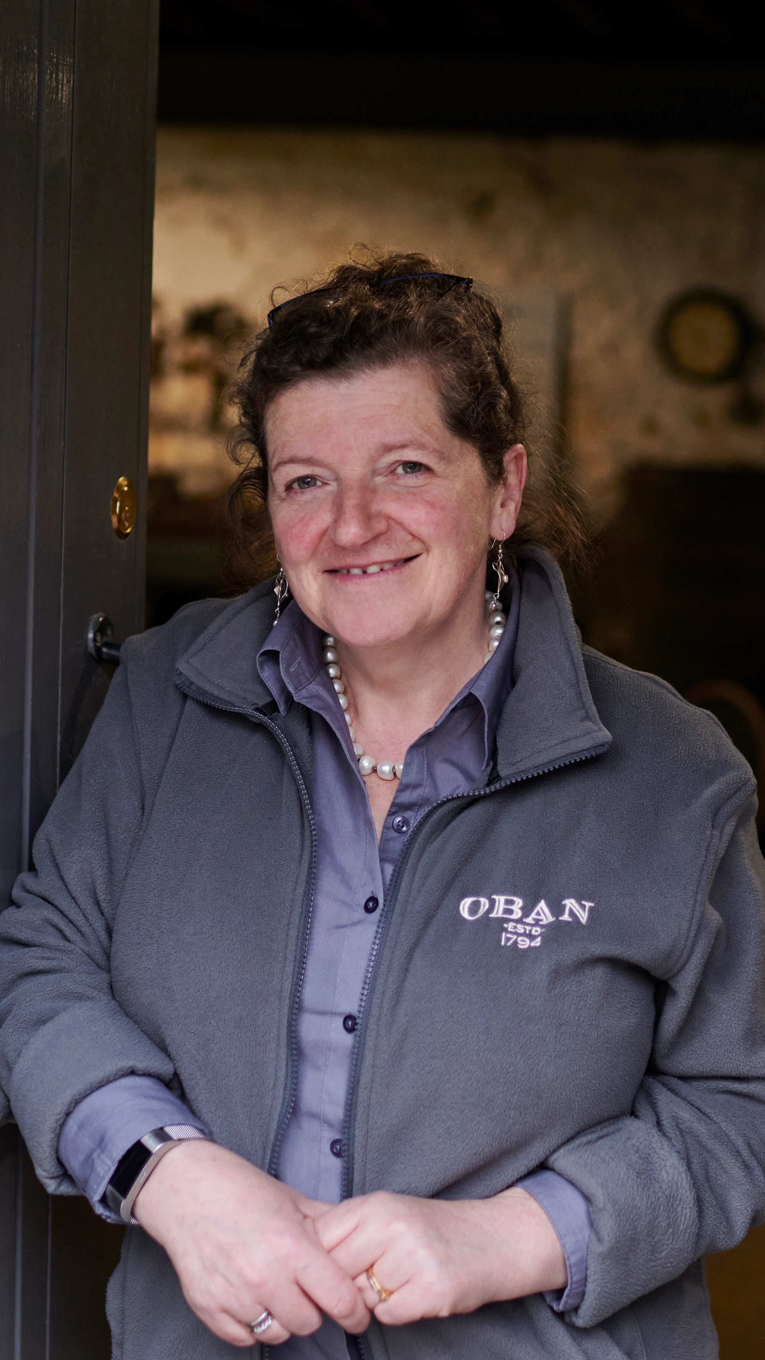 Lesley, een reisleidster van Oban, staat in een opslagruimte in de distilleerderij en draagt een grijze jas met het merk Oban.