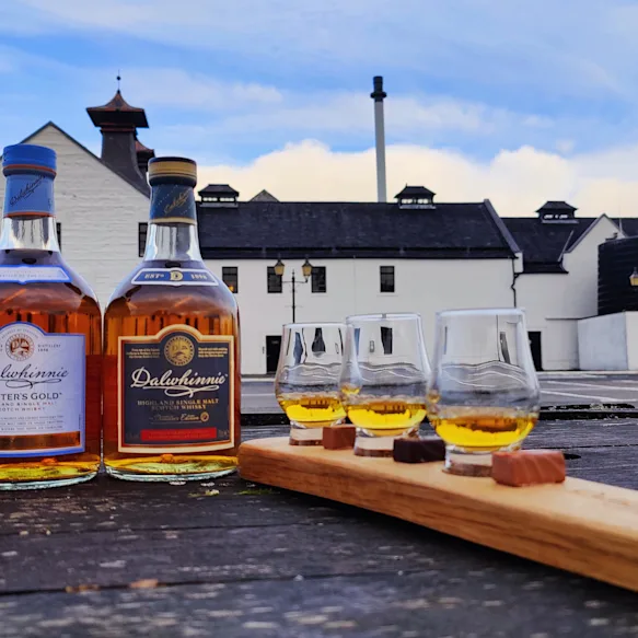Dalwhinnie Whisky tasting board paired with chocolate and three bottles of Dalwhinnie whisky. Dalwhinnie Distillery in the background.