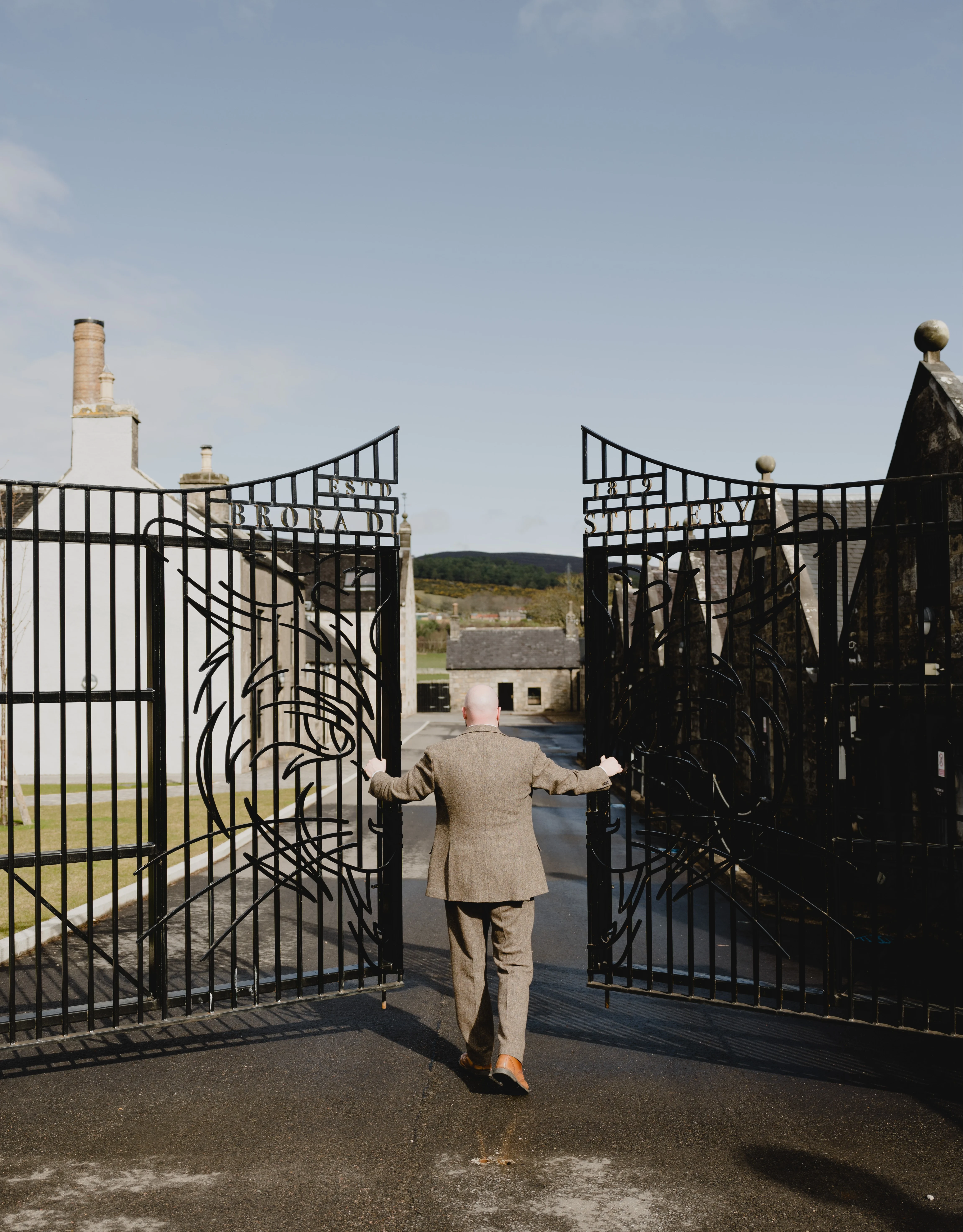A man in a suit pushes open the wrought iron gates to the Cardhu distillery.