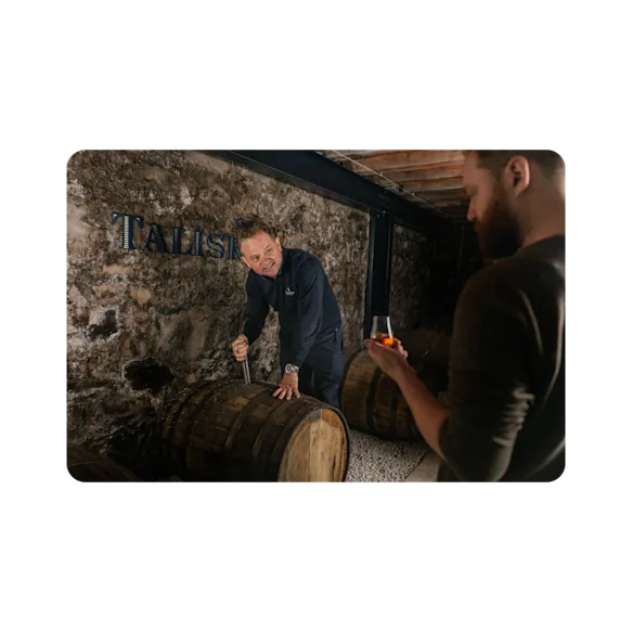 A man taps open a cask and shares a dram of Talisker with a man on the experience.