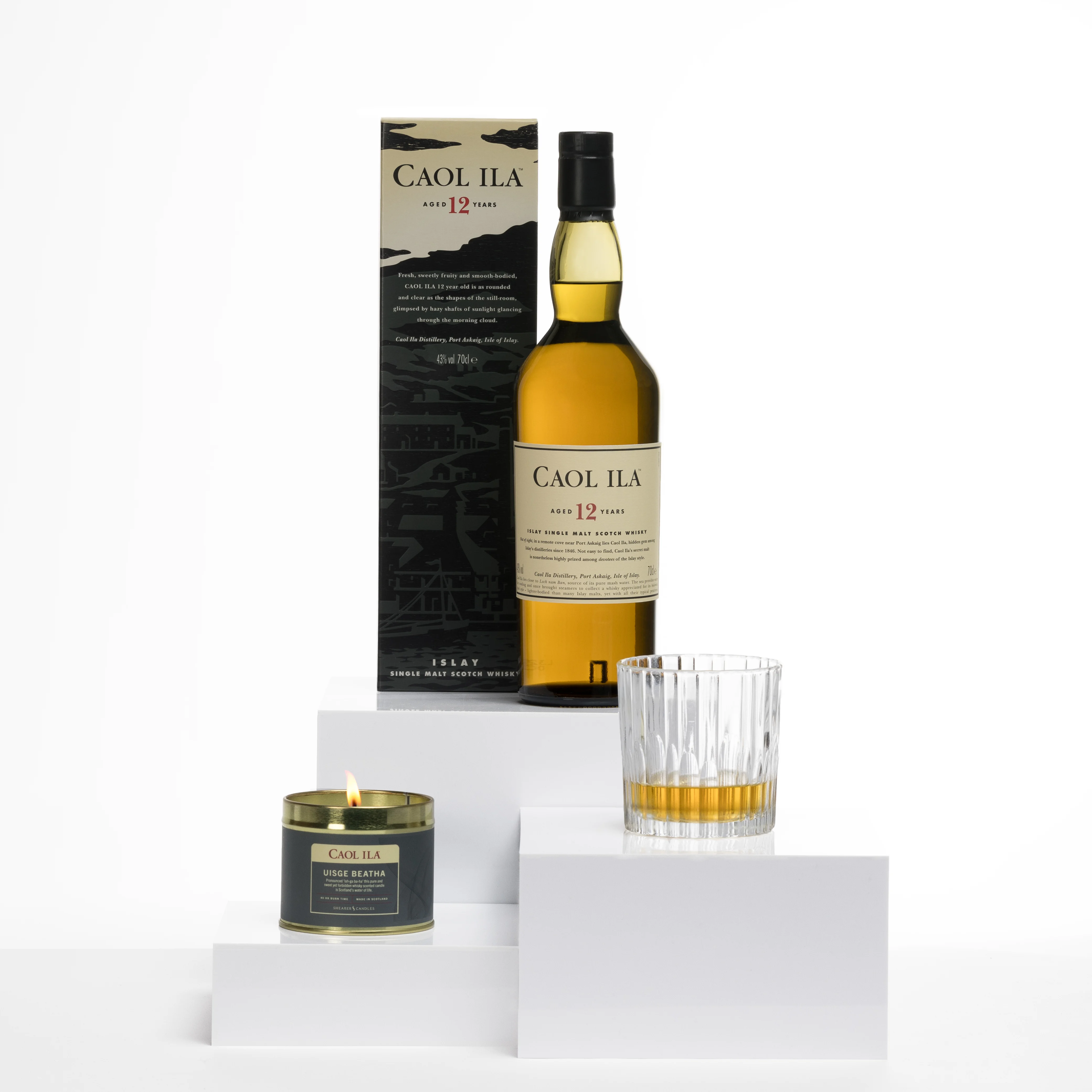 Caol Ila 12 Year Old Whiskyflasche mit passender Schachtel, einem Whiskyglas und einer brennenden Whisky-Duftkerze auf weißen Display-Blöcken.