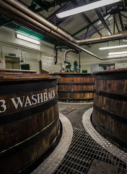 Three wooden whisky washbacks are shown in a production warehouse