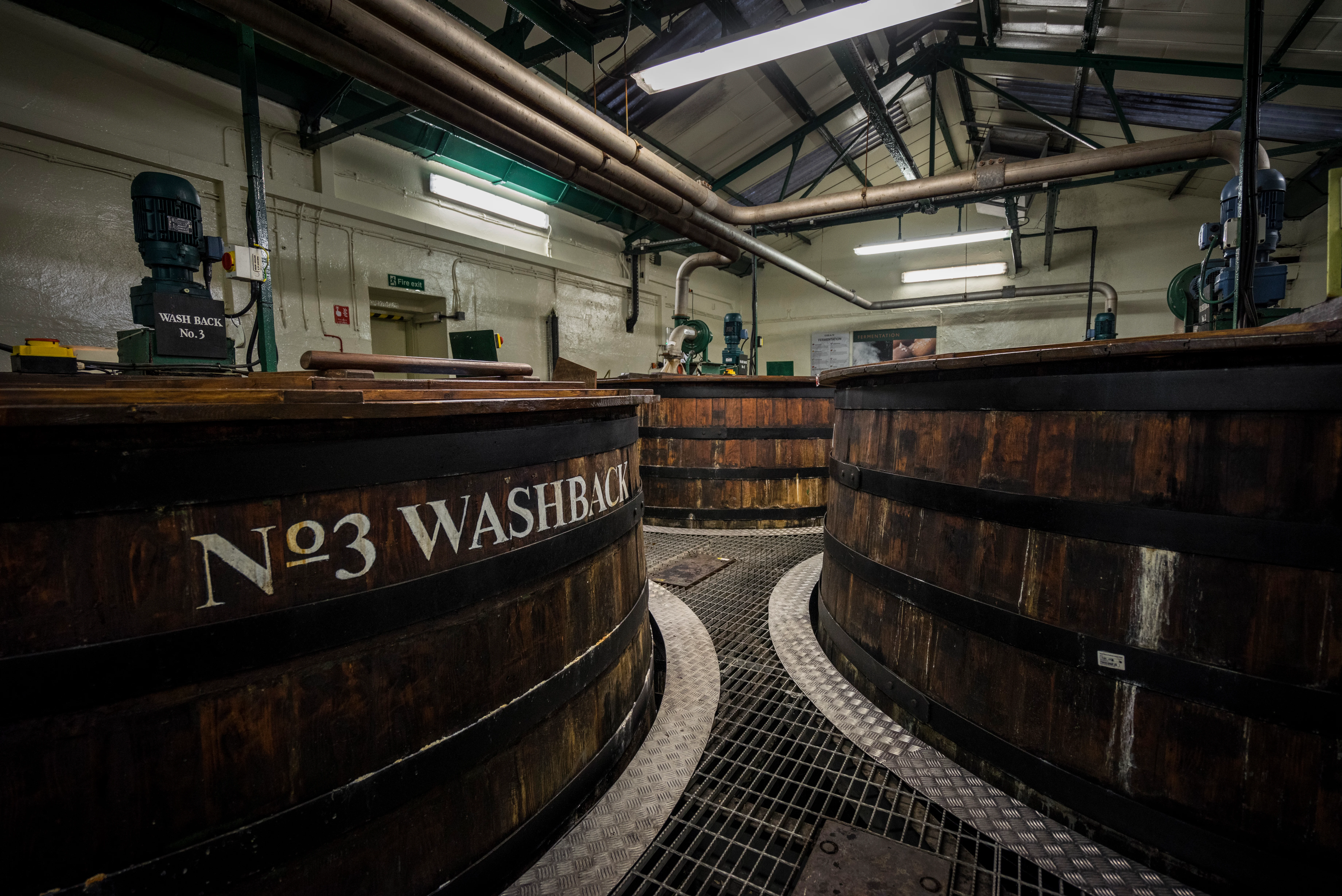 Three wooden whisky washbacks are shown in a production warehouse