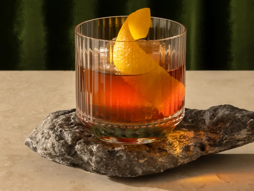 A cocktail in a rocks glass with a large twisted orange peel garnish