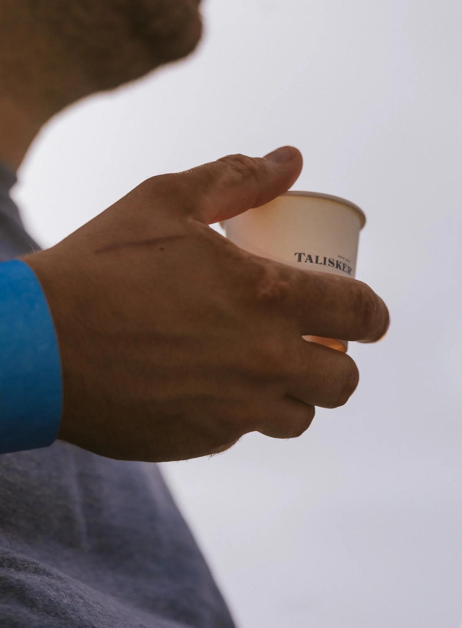 Een hand houdt een papieren beker vast met Talisker whisky erin.