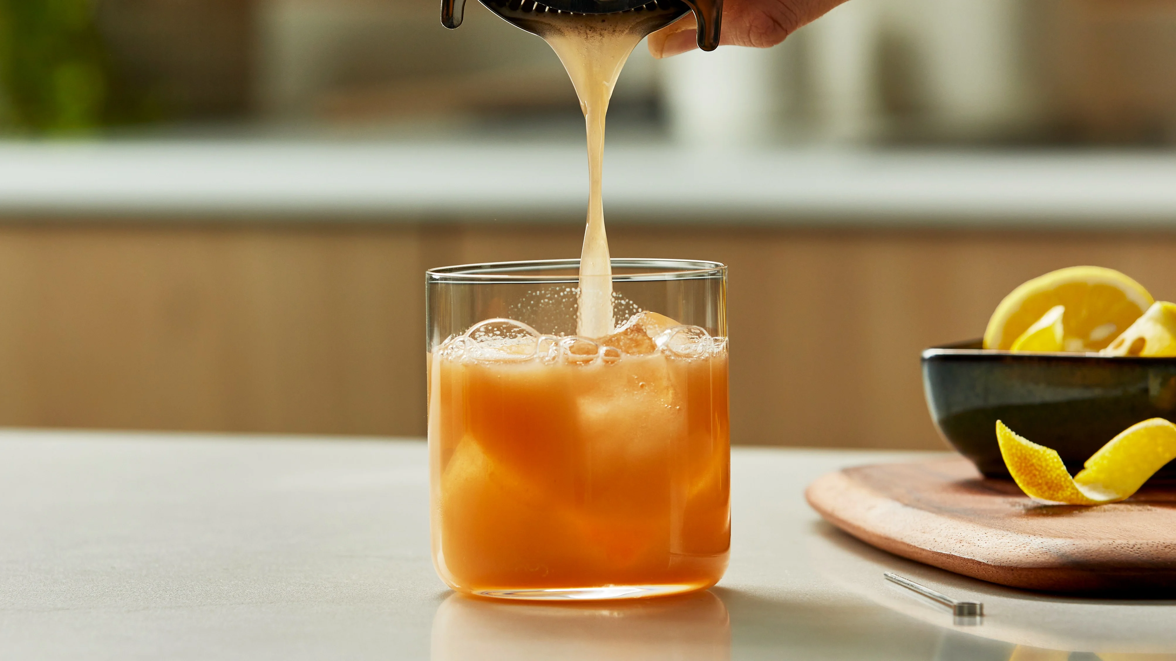 Iemand die een whisky sour in een glas met ijs schenkt