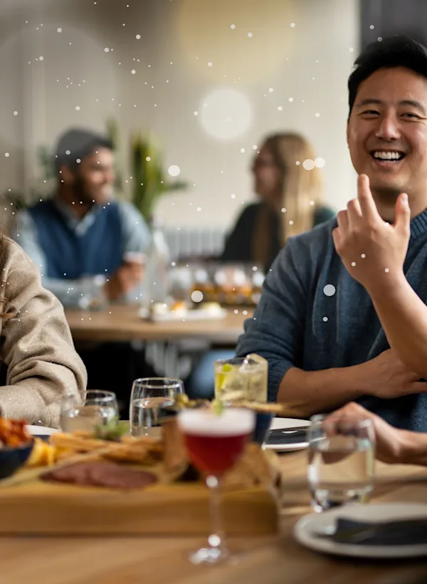 Three friends sitting around a wooden circle table with cocktails and a salame & cheese platter in the middle