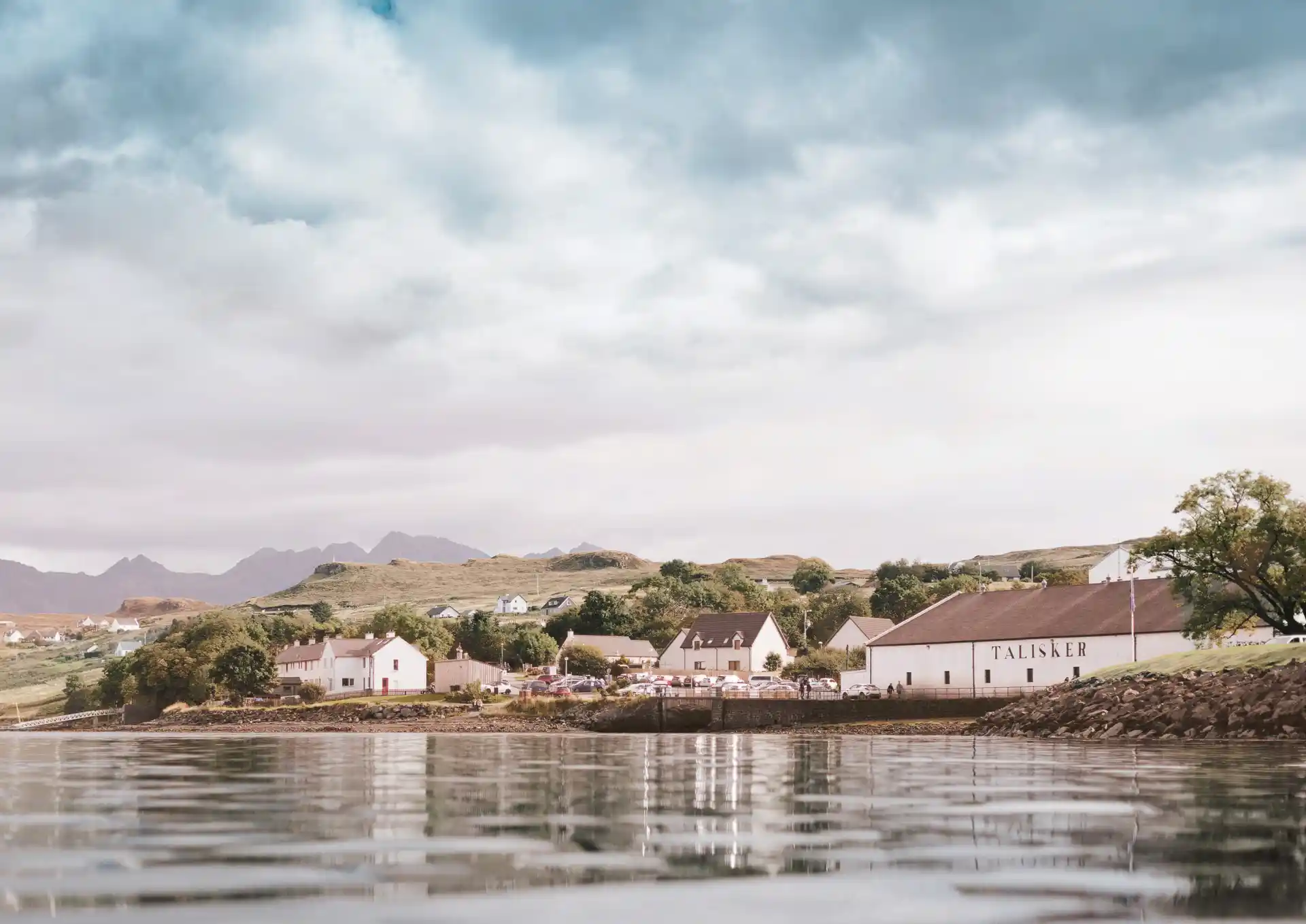 A man stood outside the distillery looking at a glass of talisker against the sky