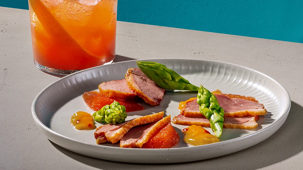 An orange-coloured whisky cocktail alongside a portion of duck breast with grapefruit chutney.